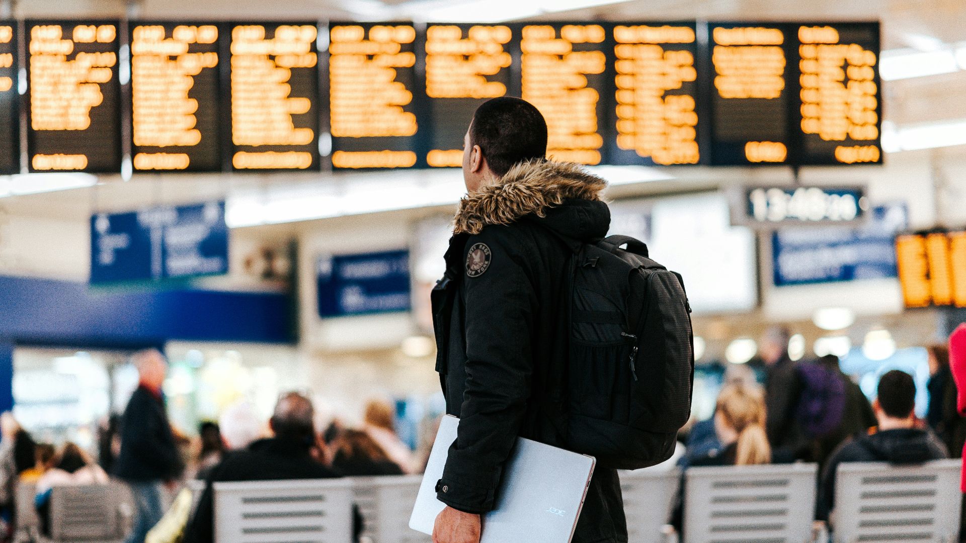 man standing inside airport looking at LED flight schedule bulletin board
