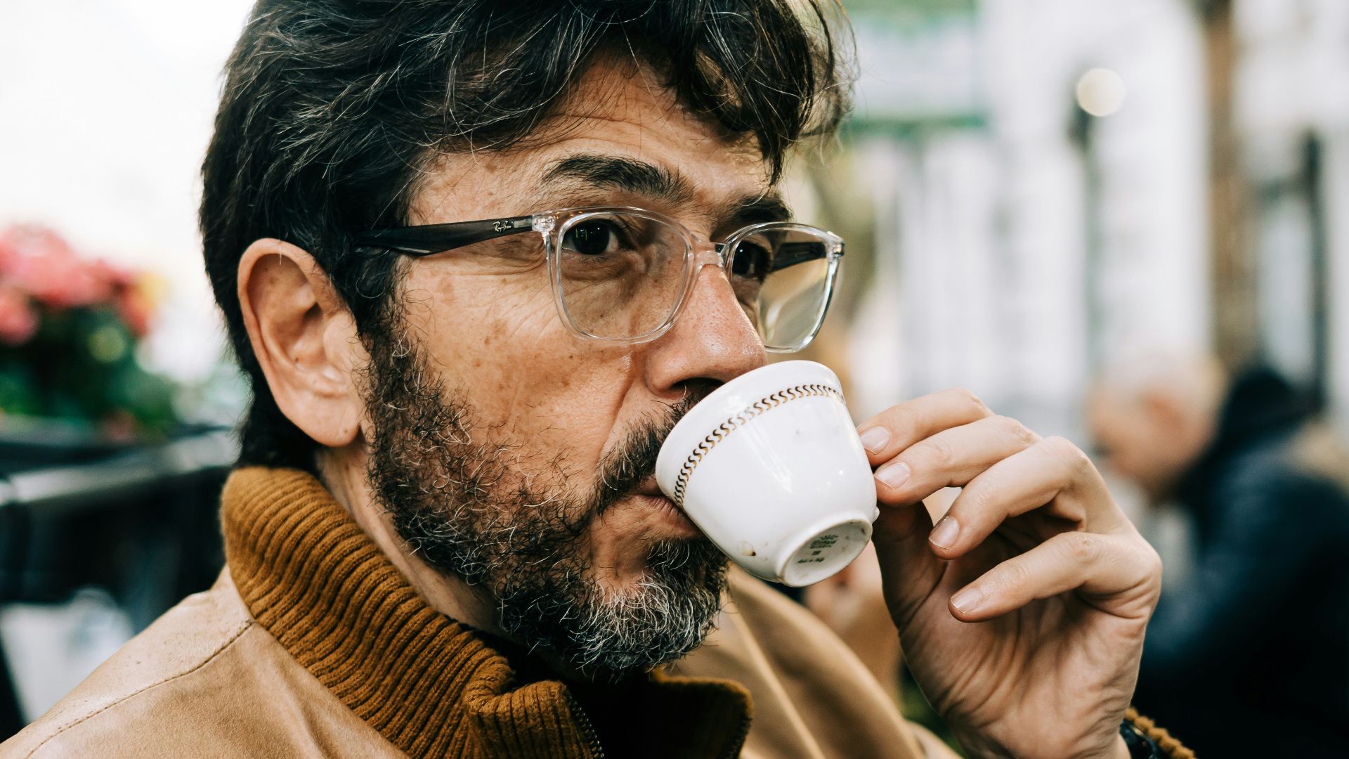man in brown jacket drinking on white ceramic mug