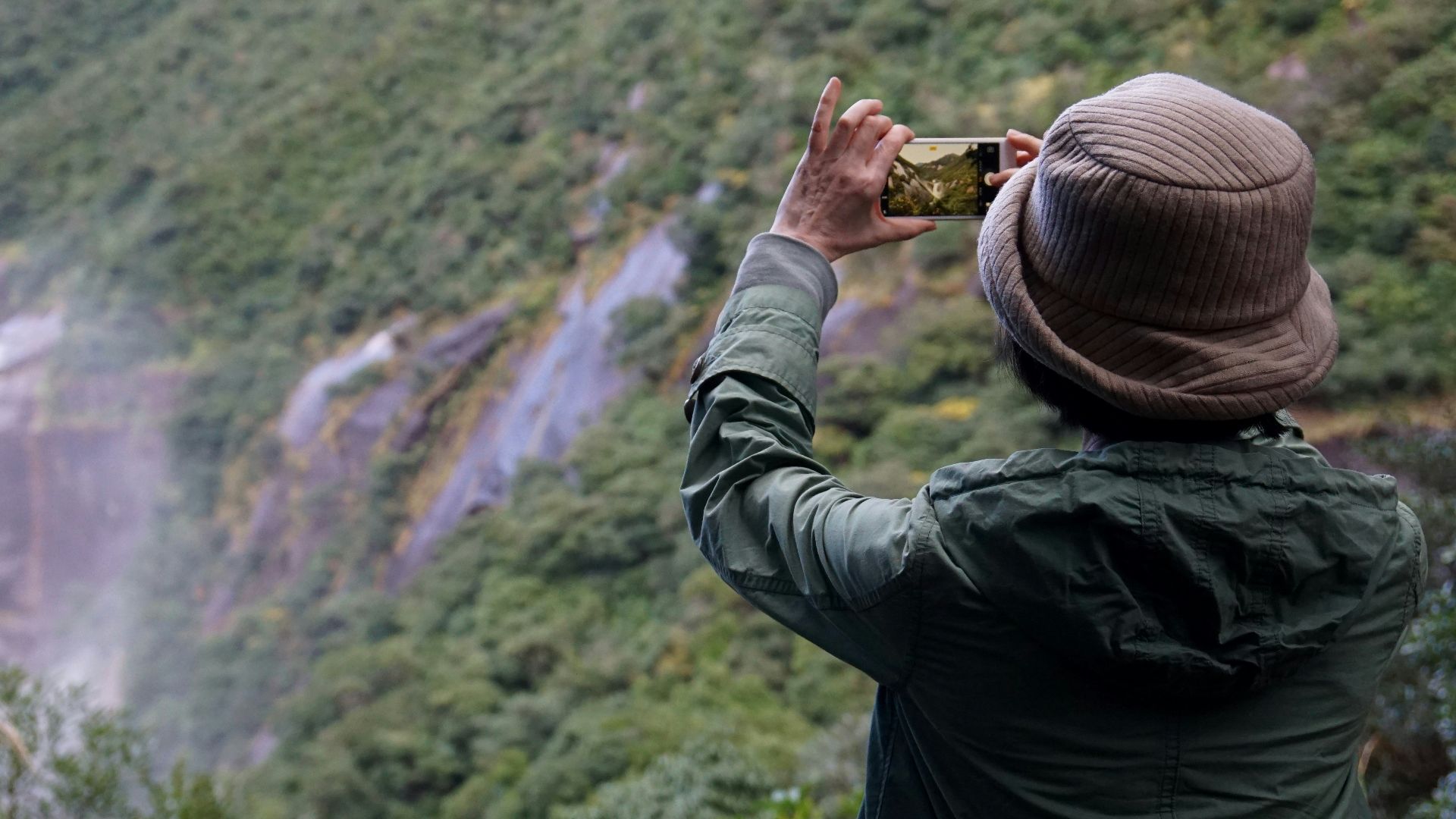 man in black jacket taking photo of waterfalls during daytime