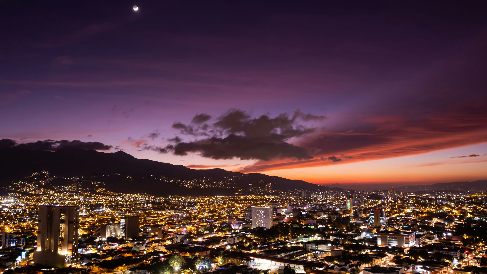 a view of a city at night with the moon in the sky