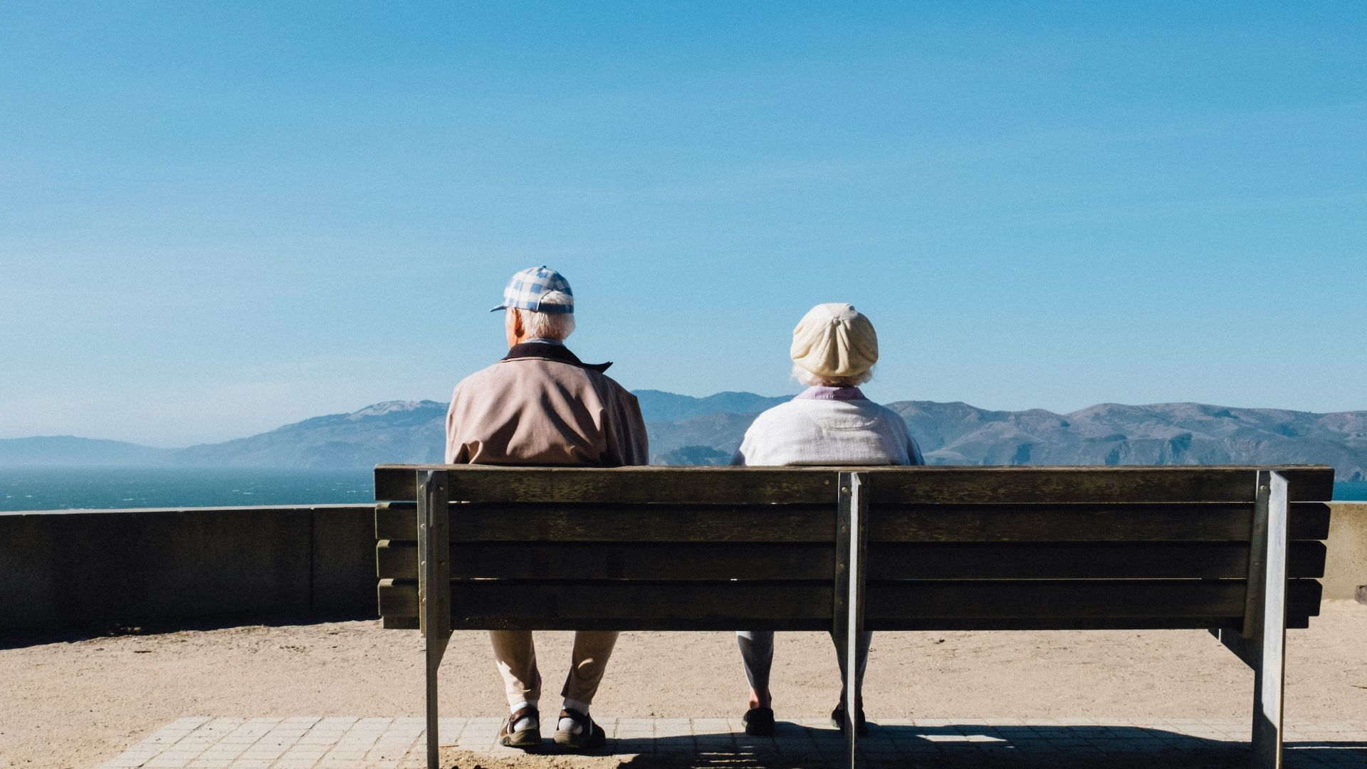 man and woman sitting on bench facing sea