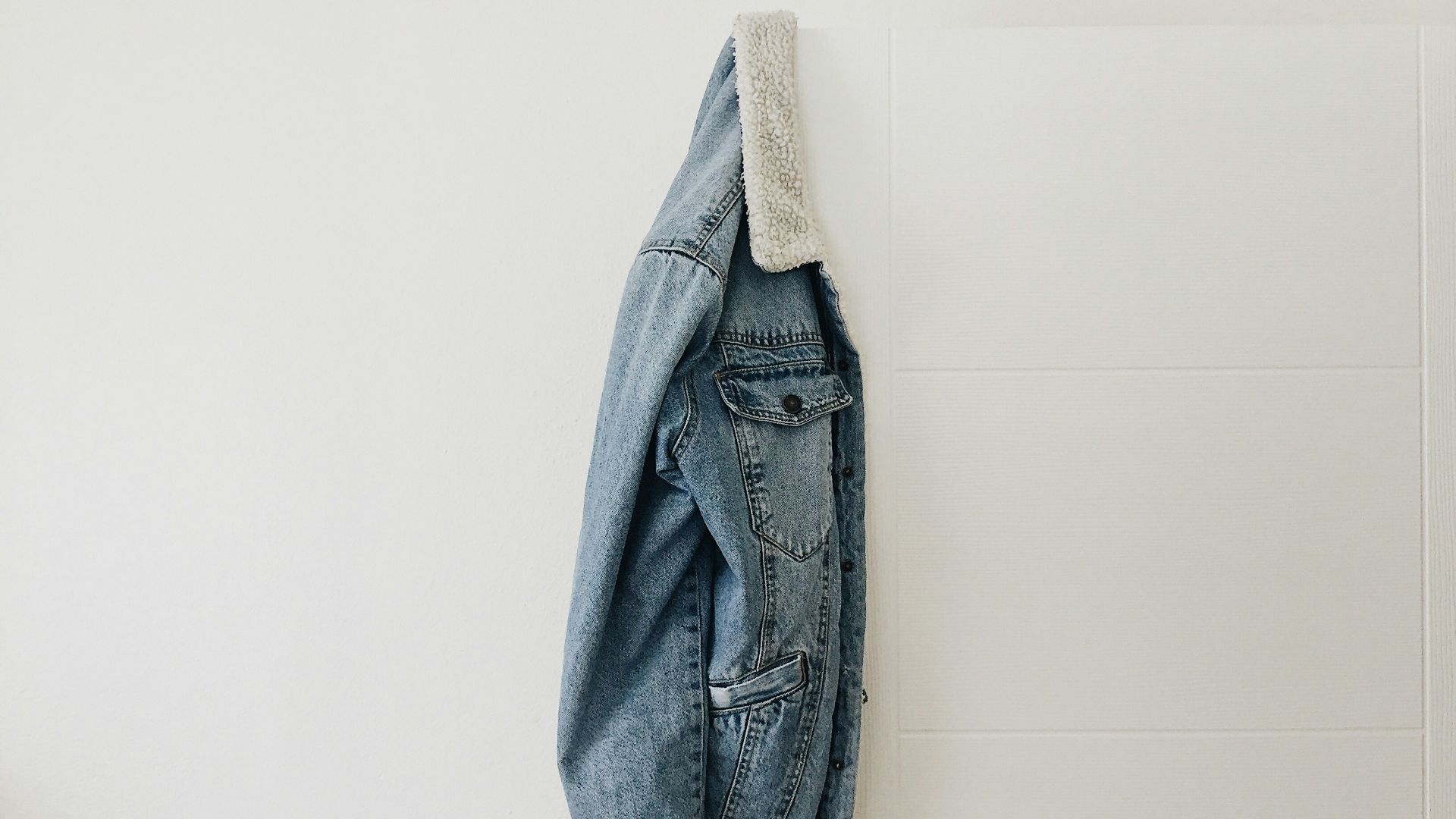 blue washed jacket hanging on white door