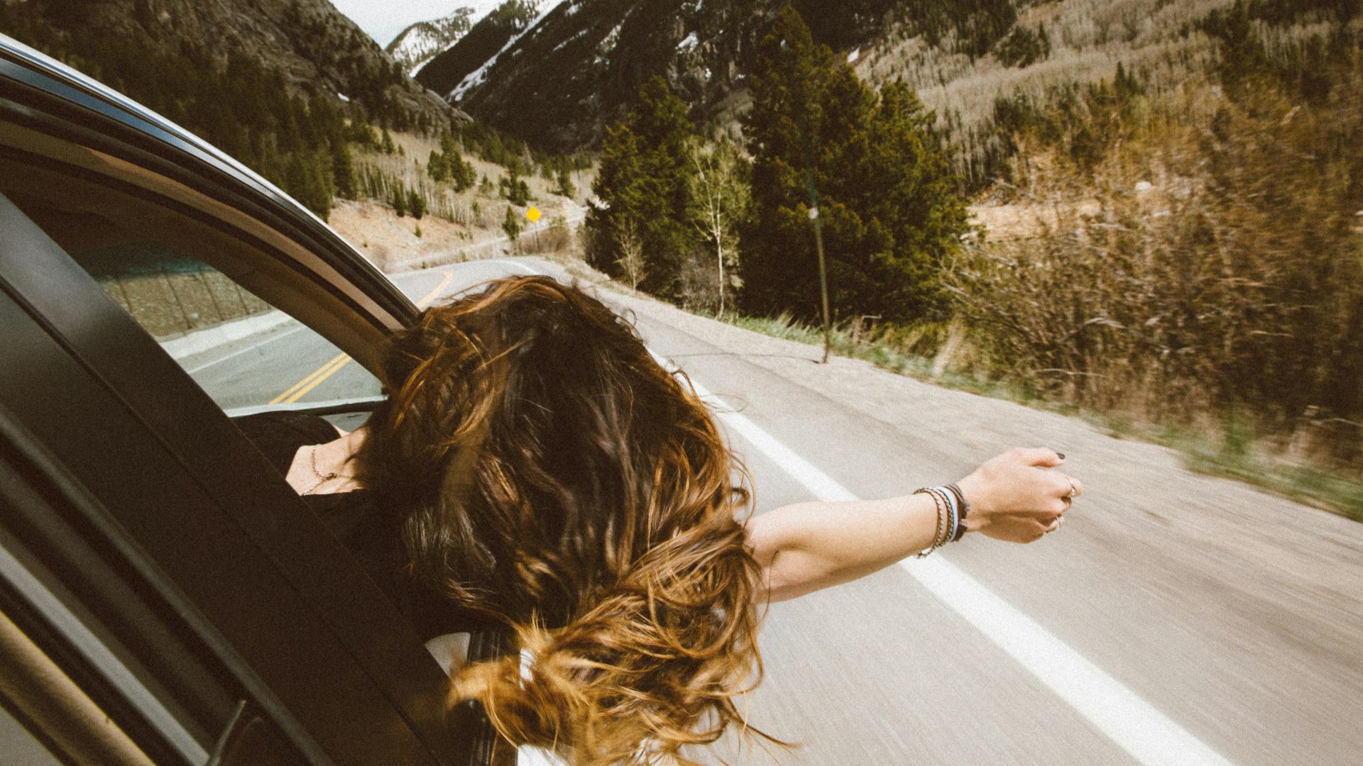 woman riding on vehicle putting her head and right arm outside the window while travelling the road