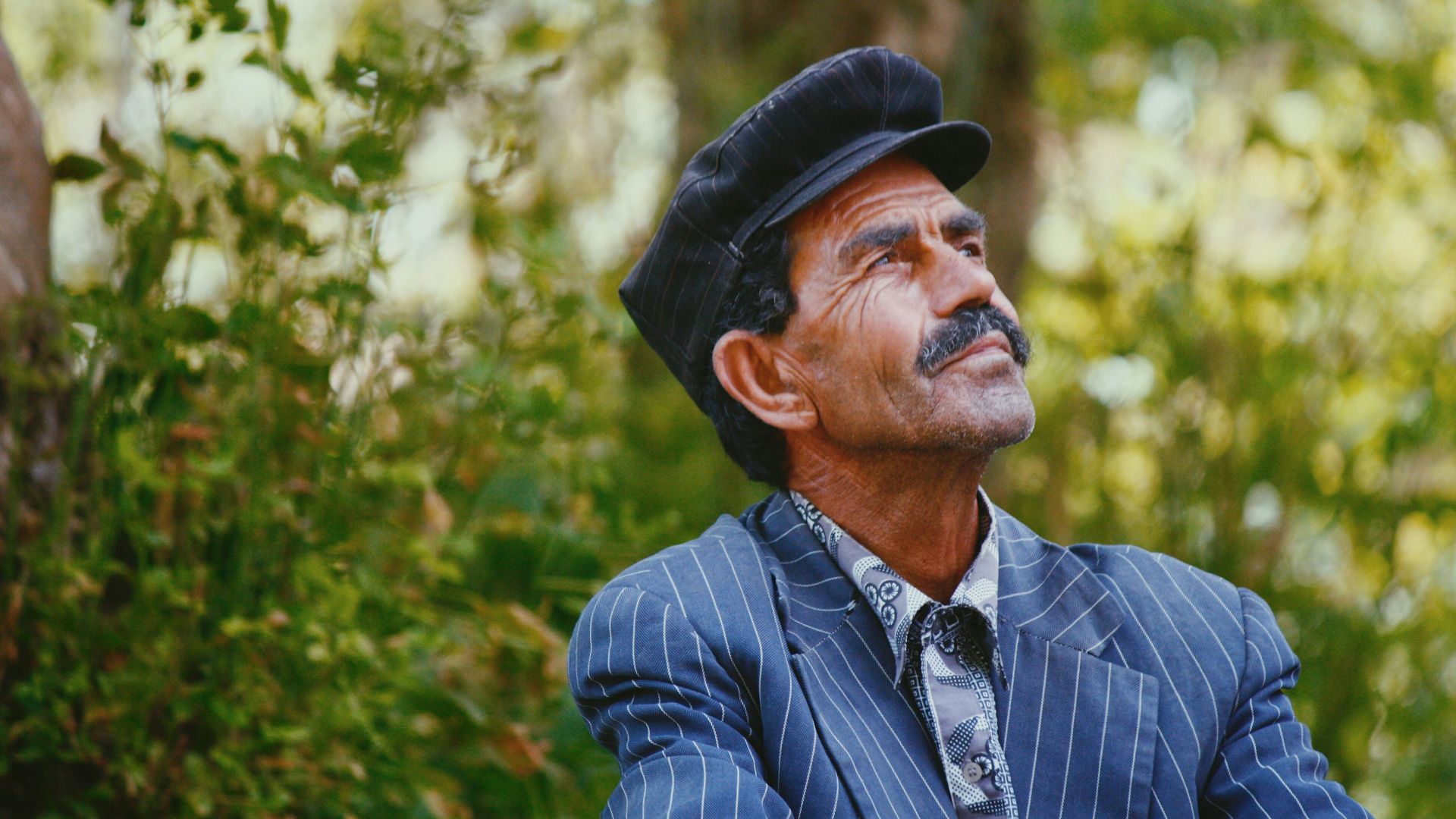 selective photo of man wearing blue shirt standing beside tree