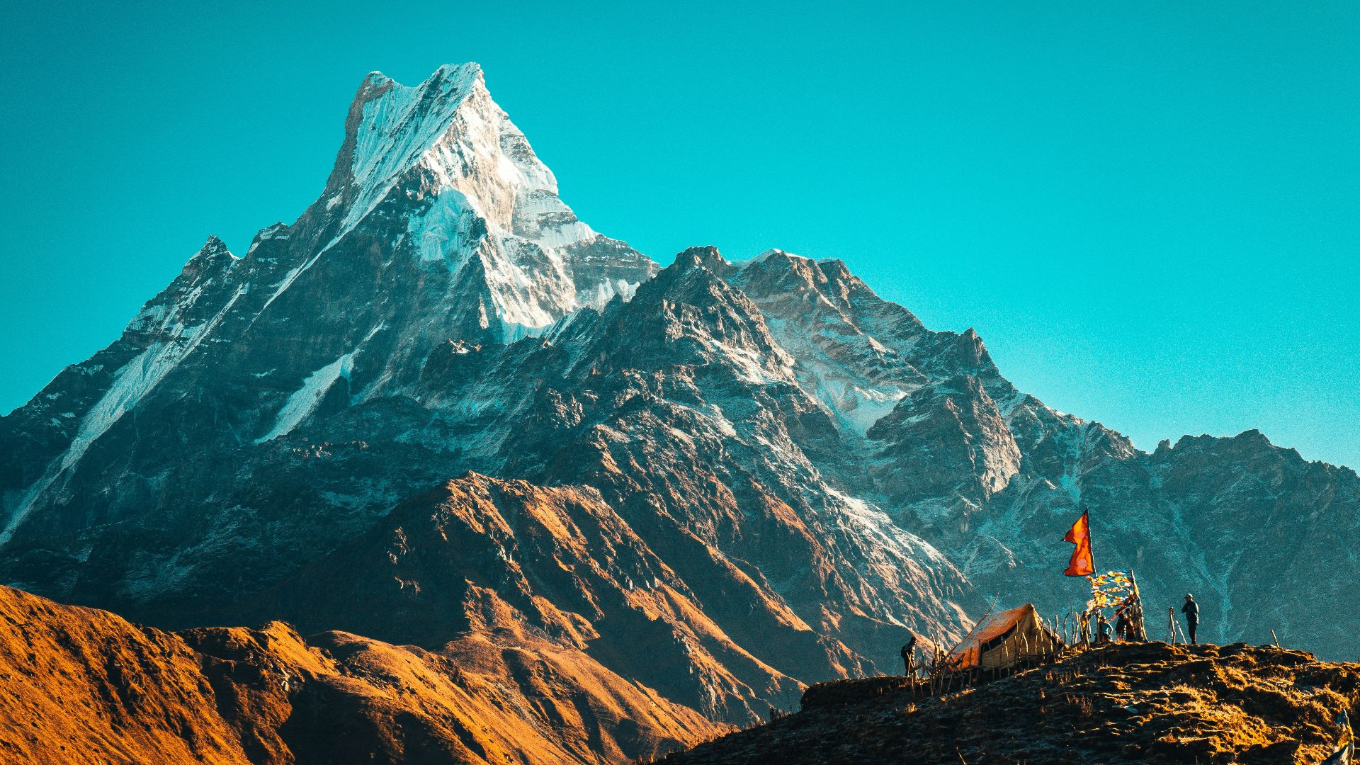 person in orange jacket standing on brown rock near snow covered mountain during daytime