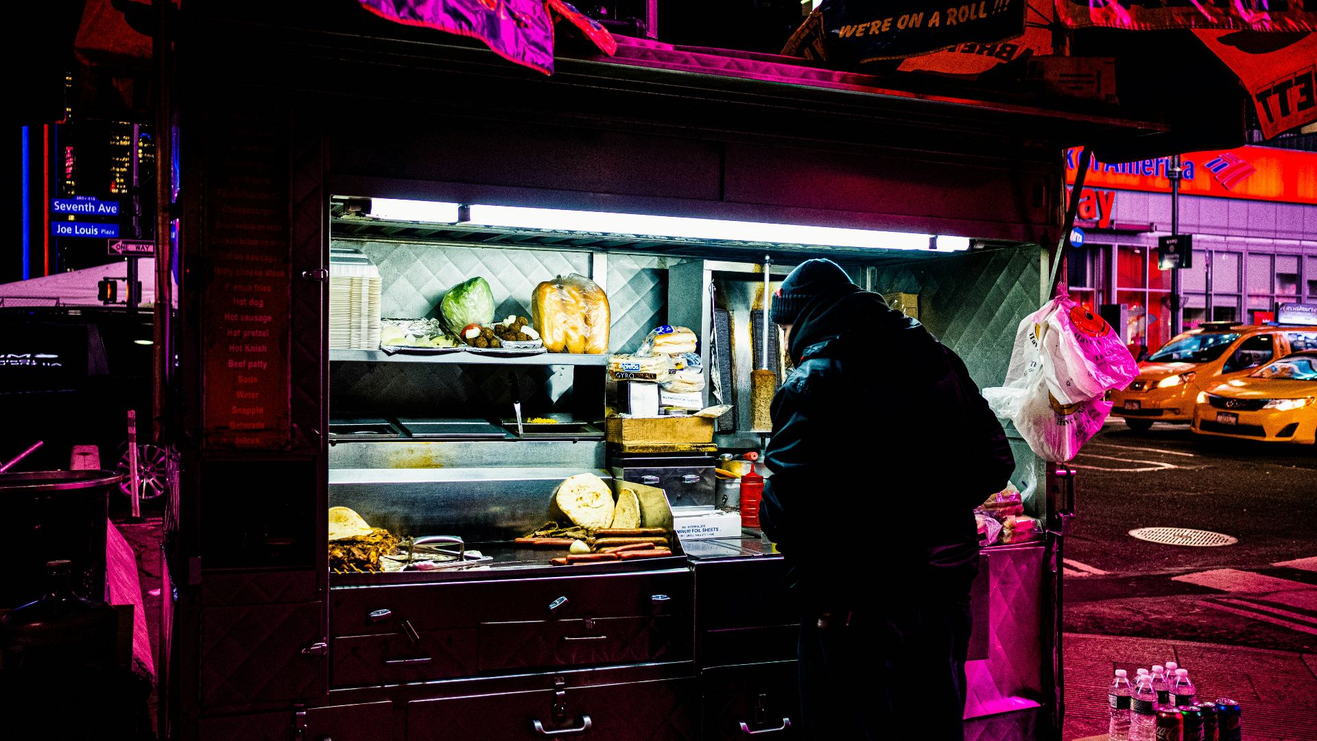man in black jacket standing in front of food stall