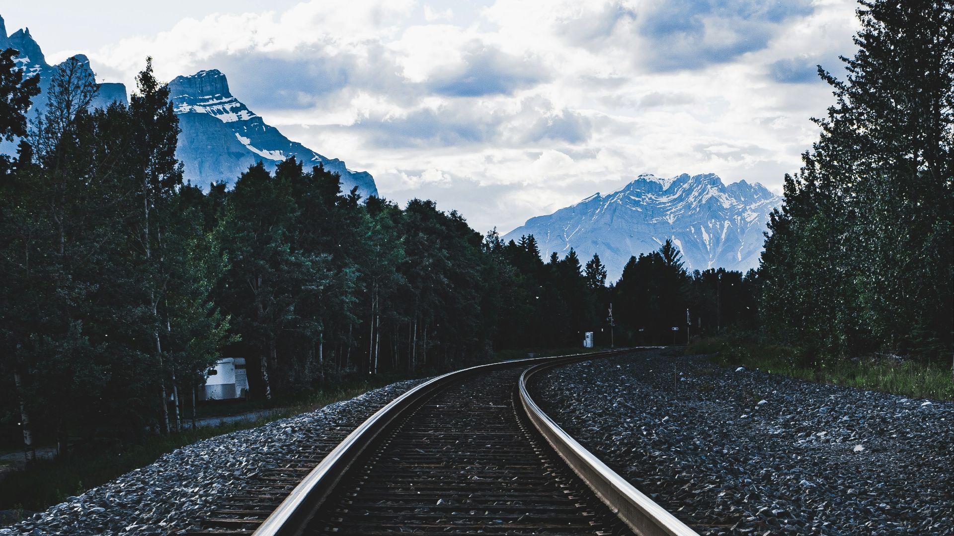 train rail near green trees under white clouds and blue sky during daytime