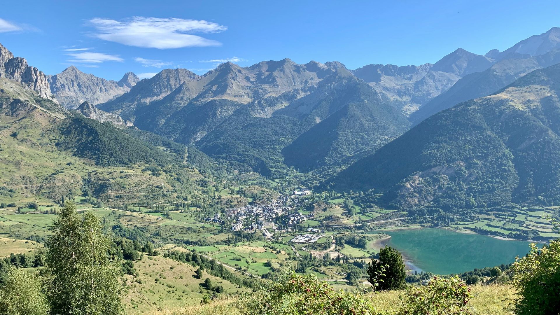 green grass field near lake and mountains under blue sky during daytime