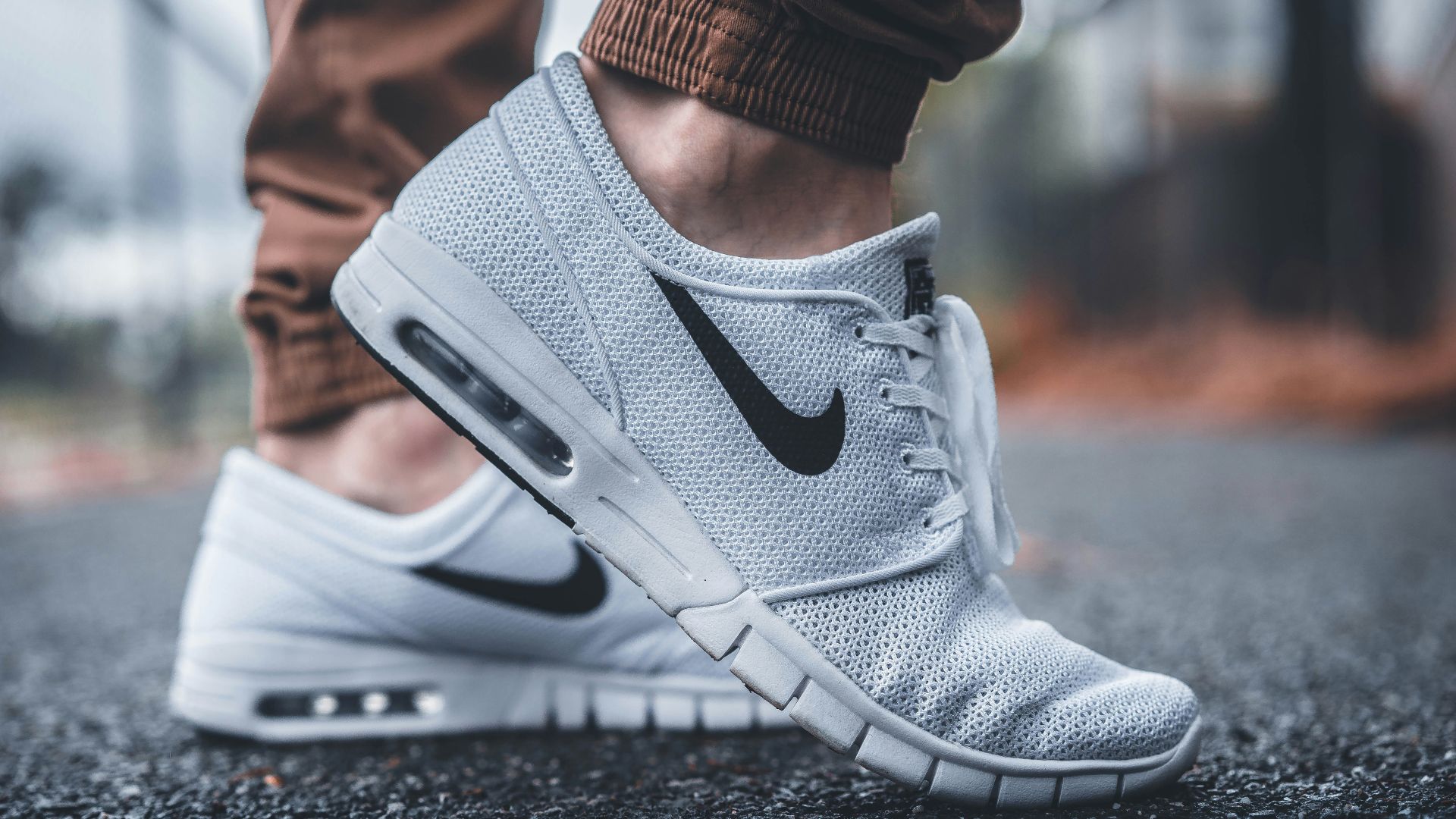 person wearing white Nike running shoes standing on black concrete path