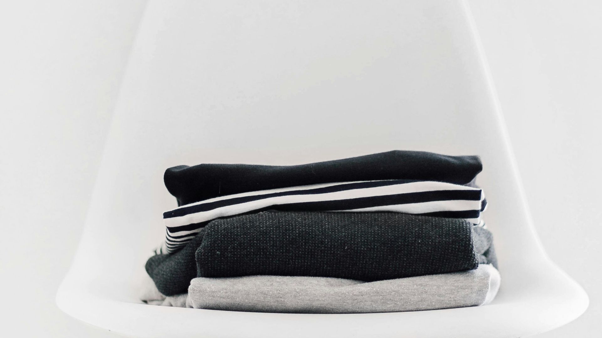 pile of black, white, and gray textiles on white padded chair with brown frame
