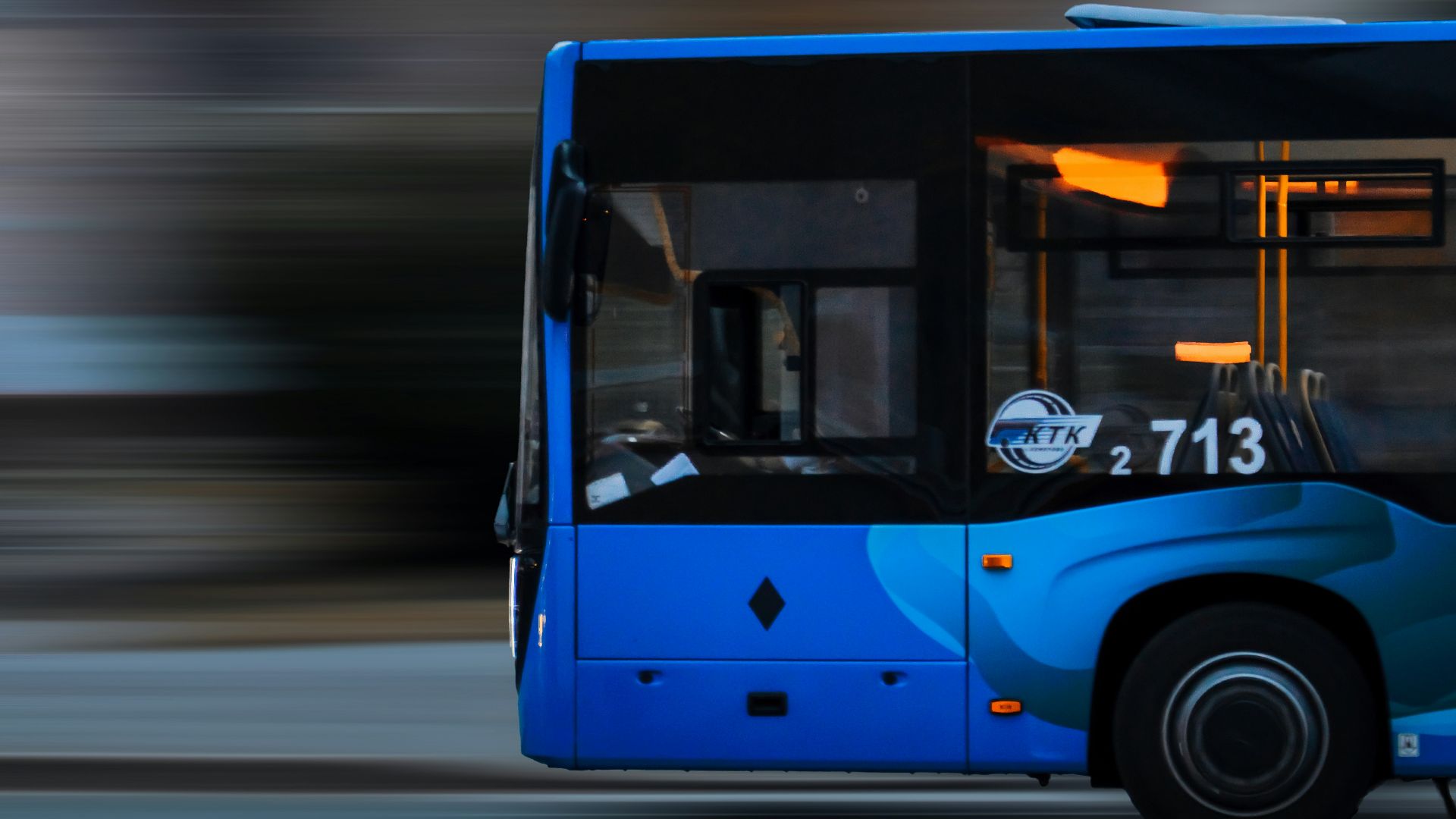 a blue bus driving down a street next to a tall building
