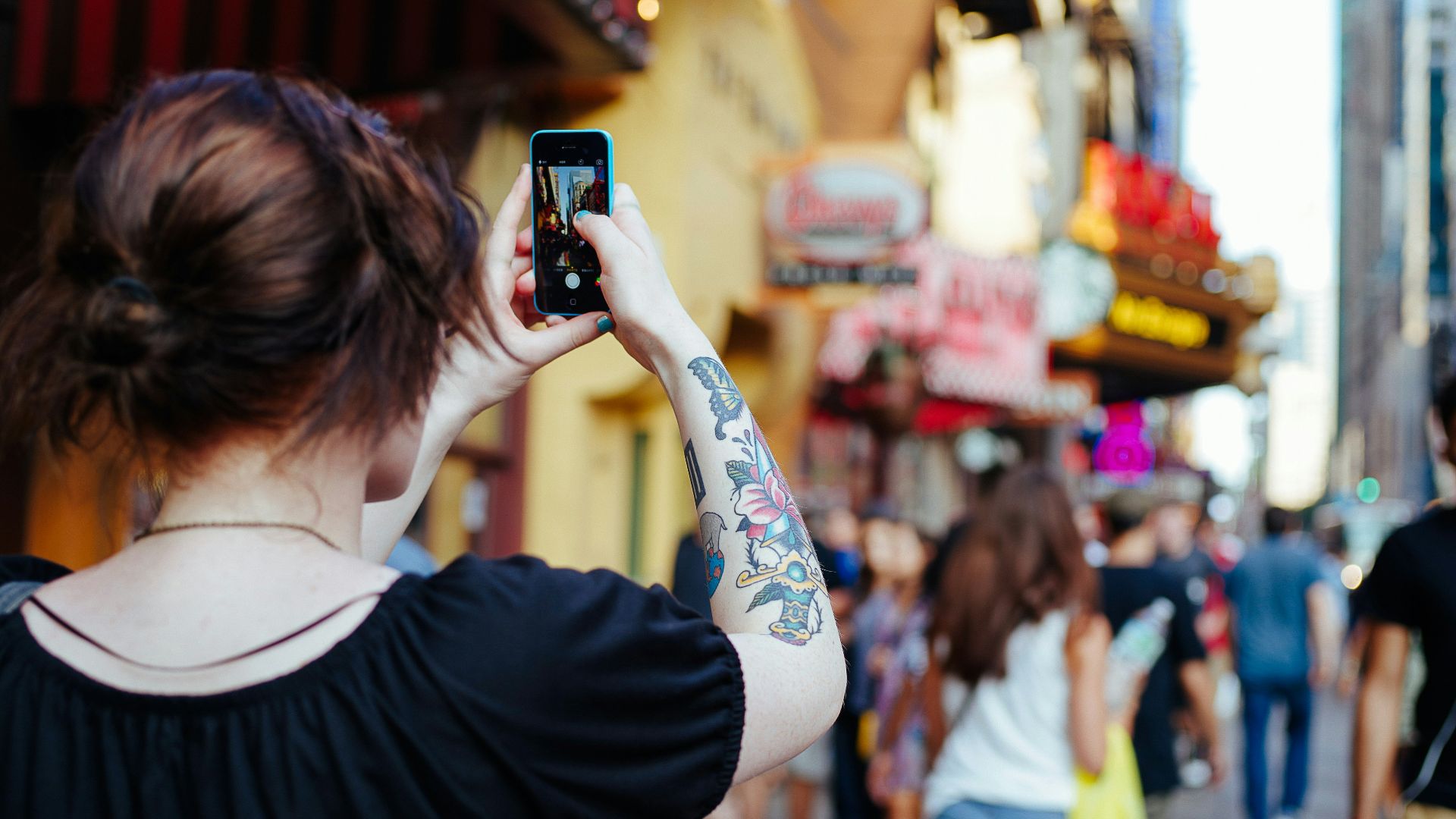 focus photo of woman in black cap-sleeved shirt holding smartphone while taking photo