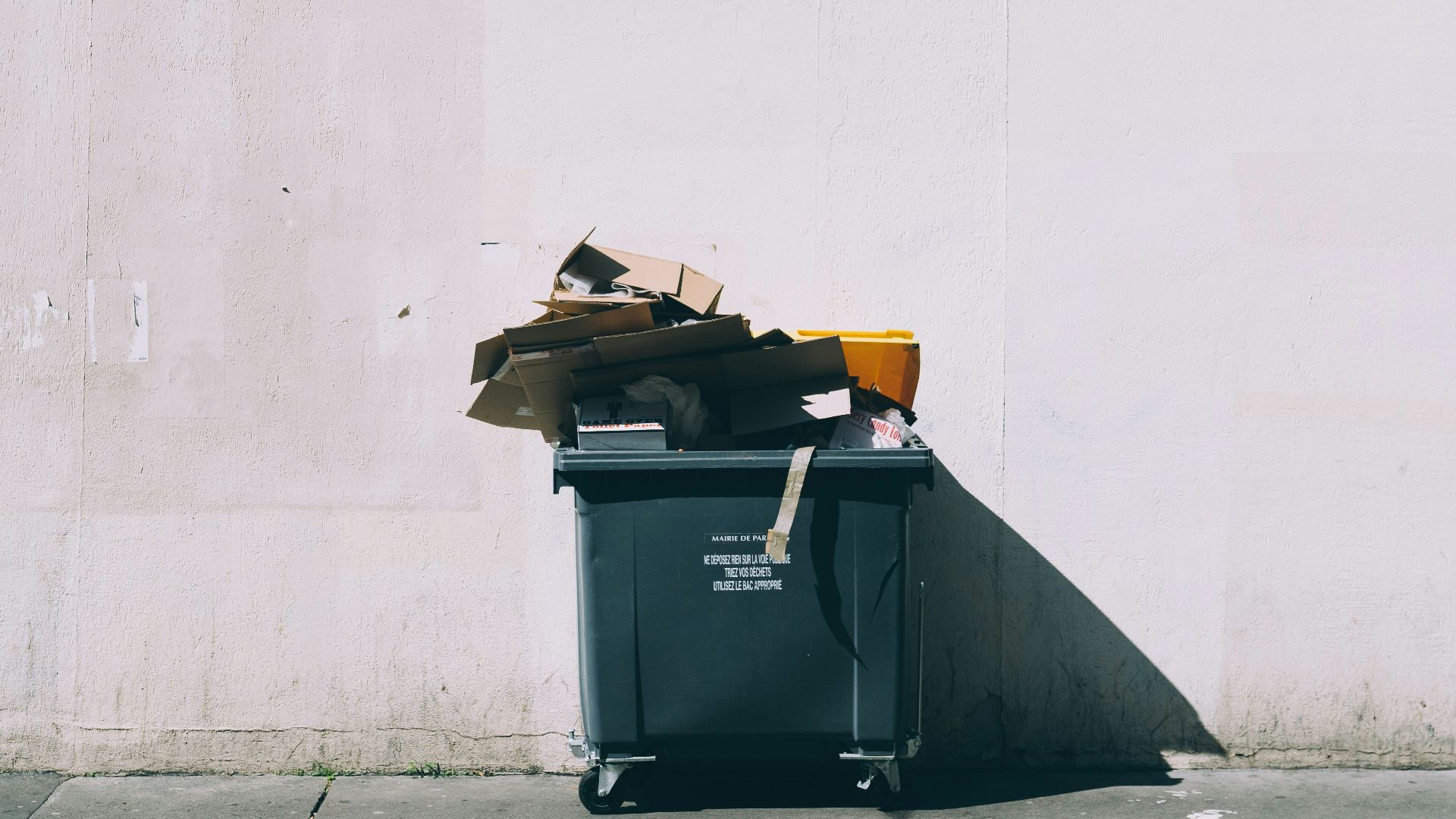 black plastic garbage bin with wheels beside wall
