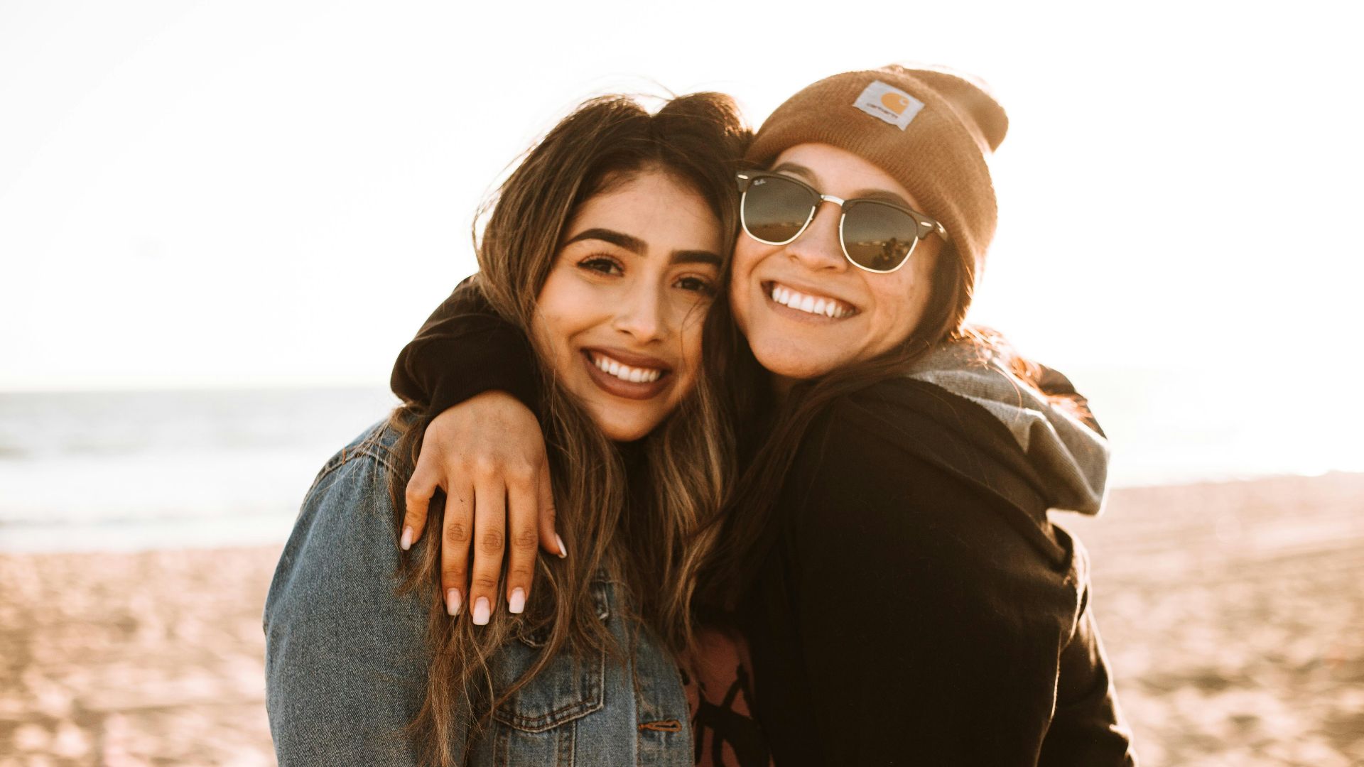 woman hugging other woman while smiling at beach