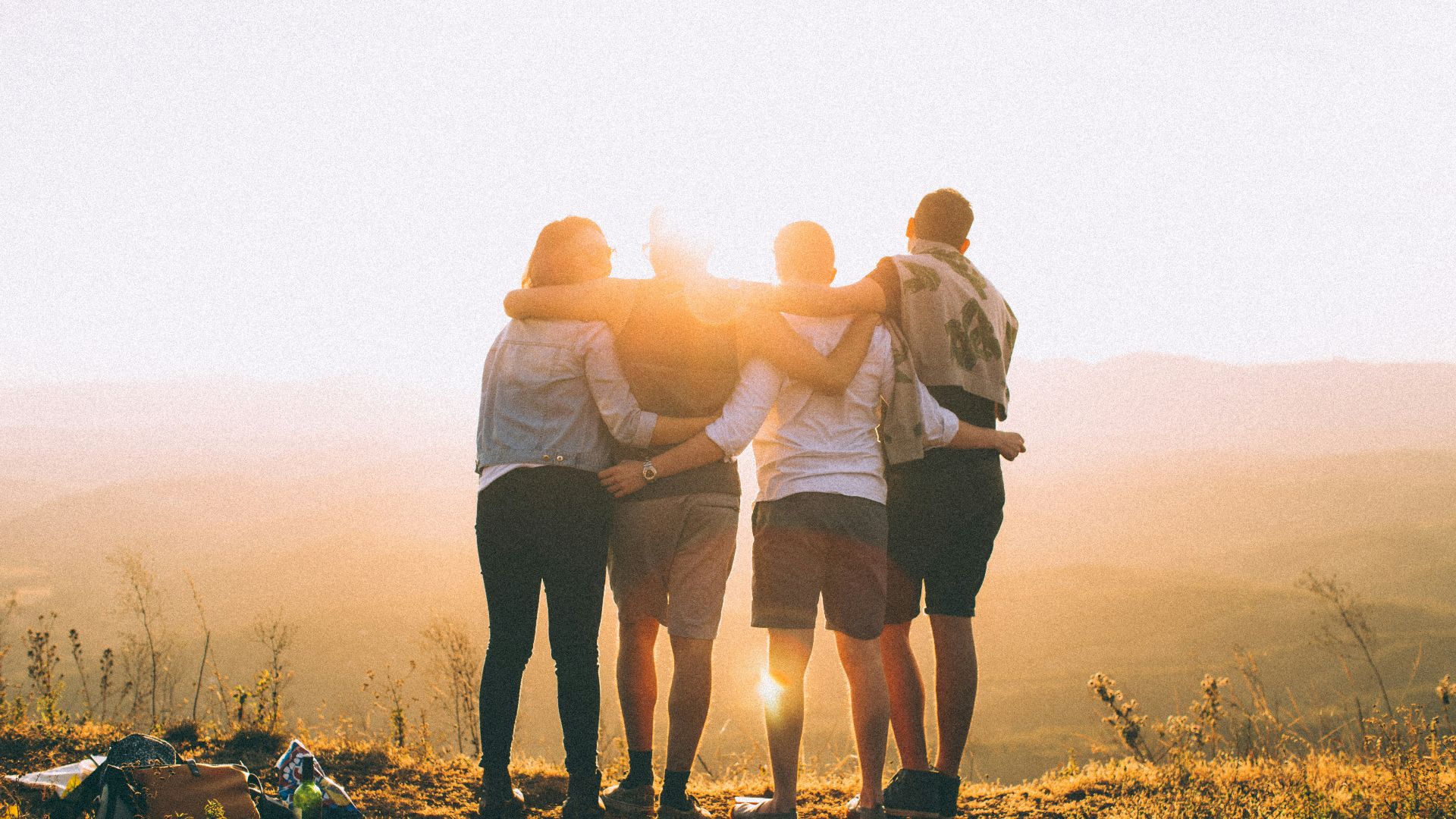 four person hands wrap around shoulders while looking at sunset
