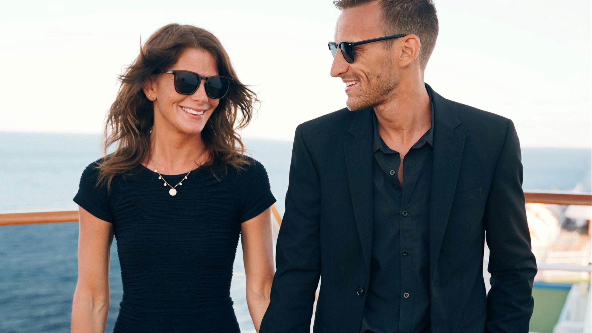a man and woman wearing sunglasses and standing on a deck