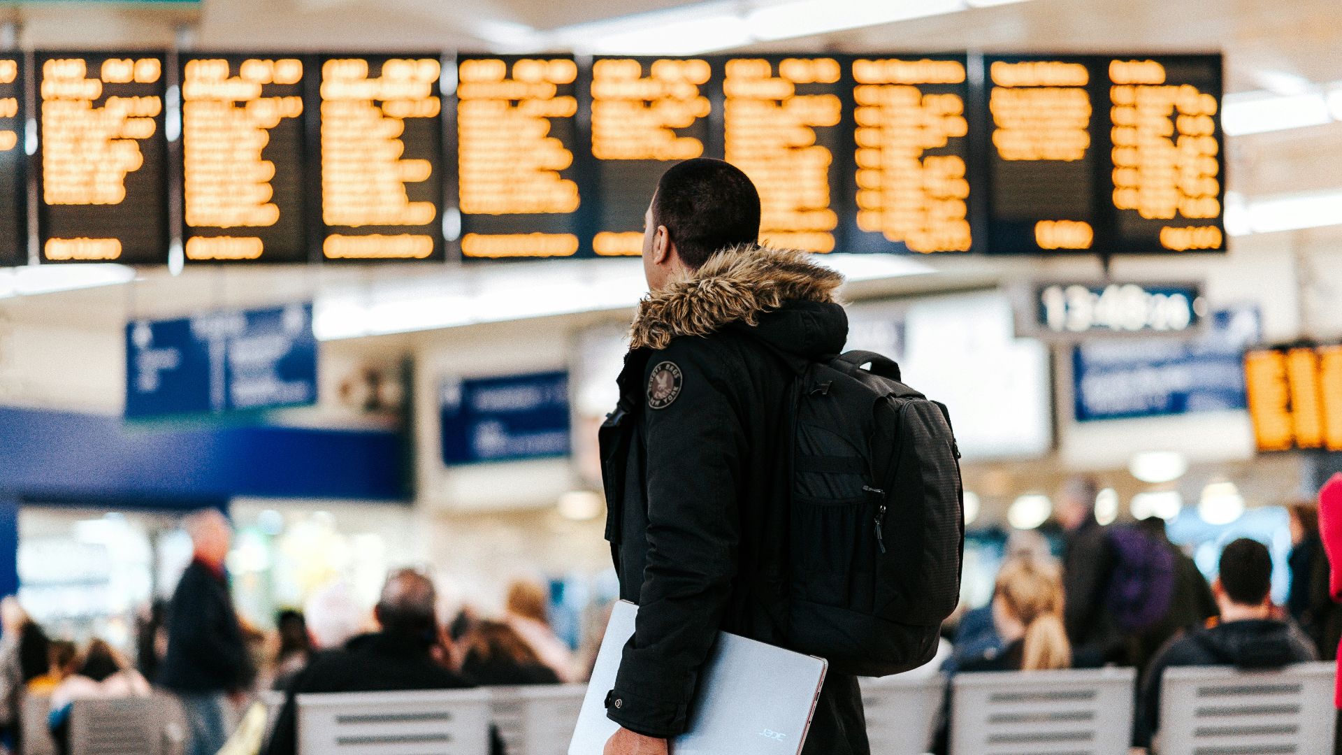 man standing inside airport looking at LED flight schedule bulletin board