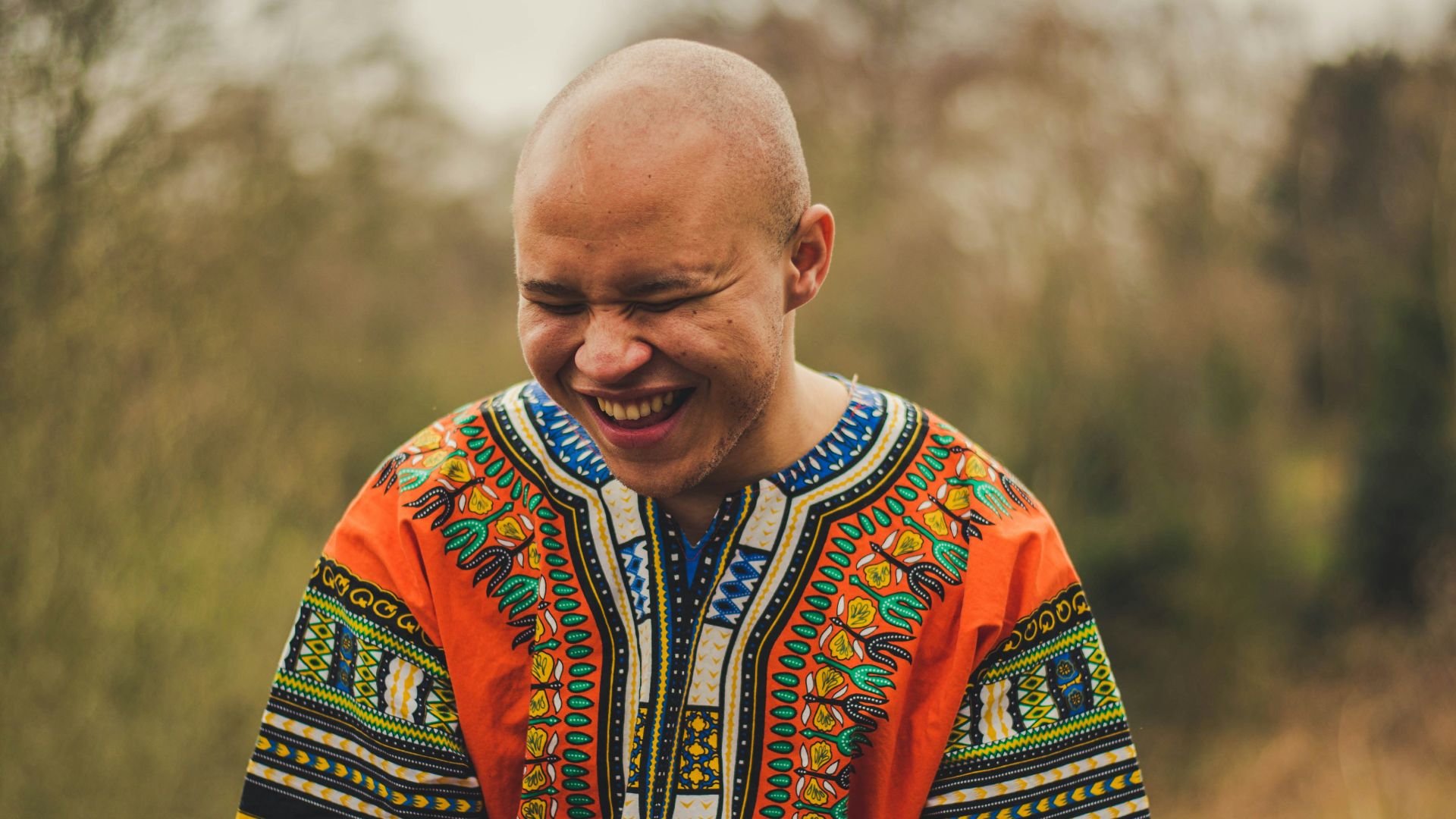 smiling man wearing orange and green daishiki shirt sitting on grey surface
