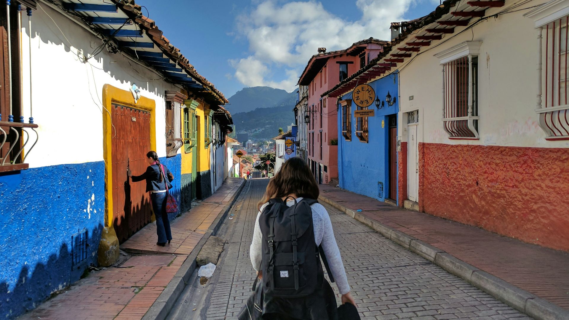 person in gray shirt with backpack walking on street between houses