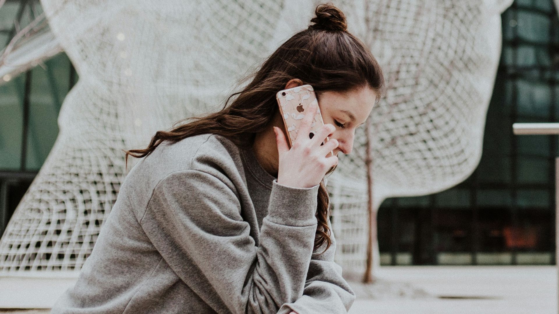 woman sitting on ground holding smartphone near building