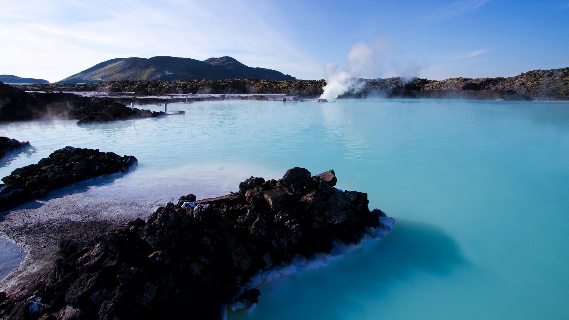 calm water beside mountain under white clouds and blue sky