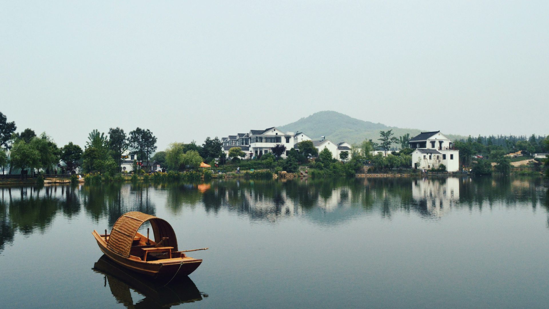 brown wooden boat on body of water overlooking houses by the shore at daytime