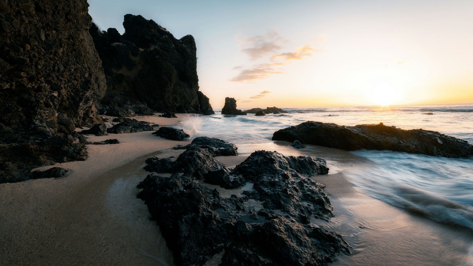 the sun is setting over the ocean and rocks
