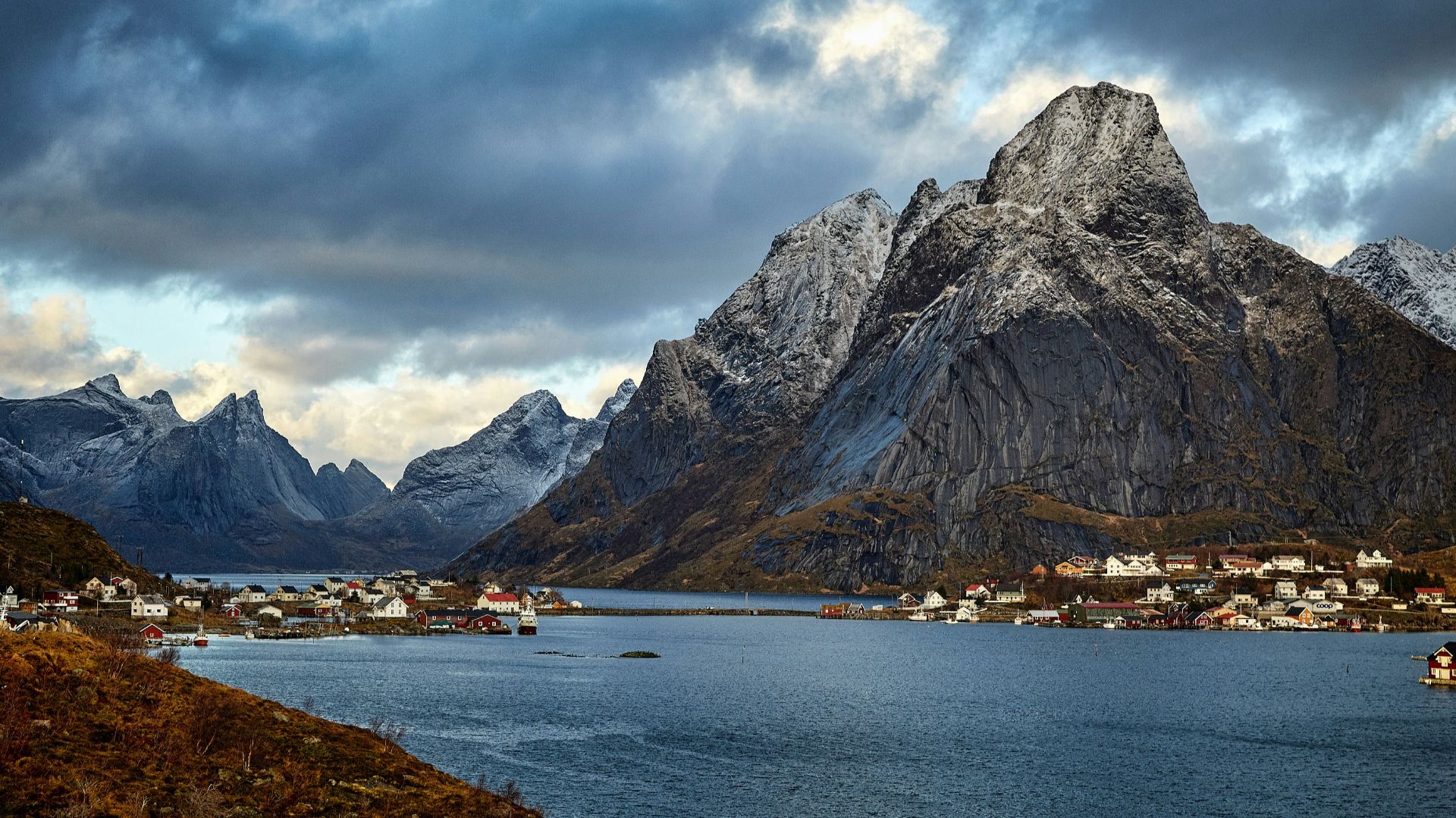 body of water near rock mountain under cloudy skies