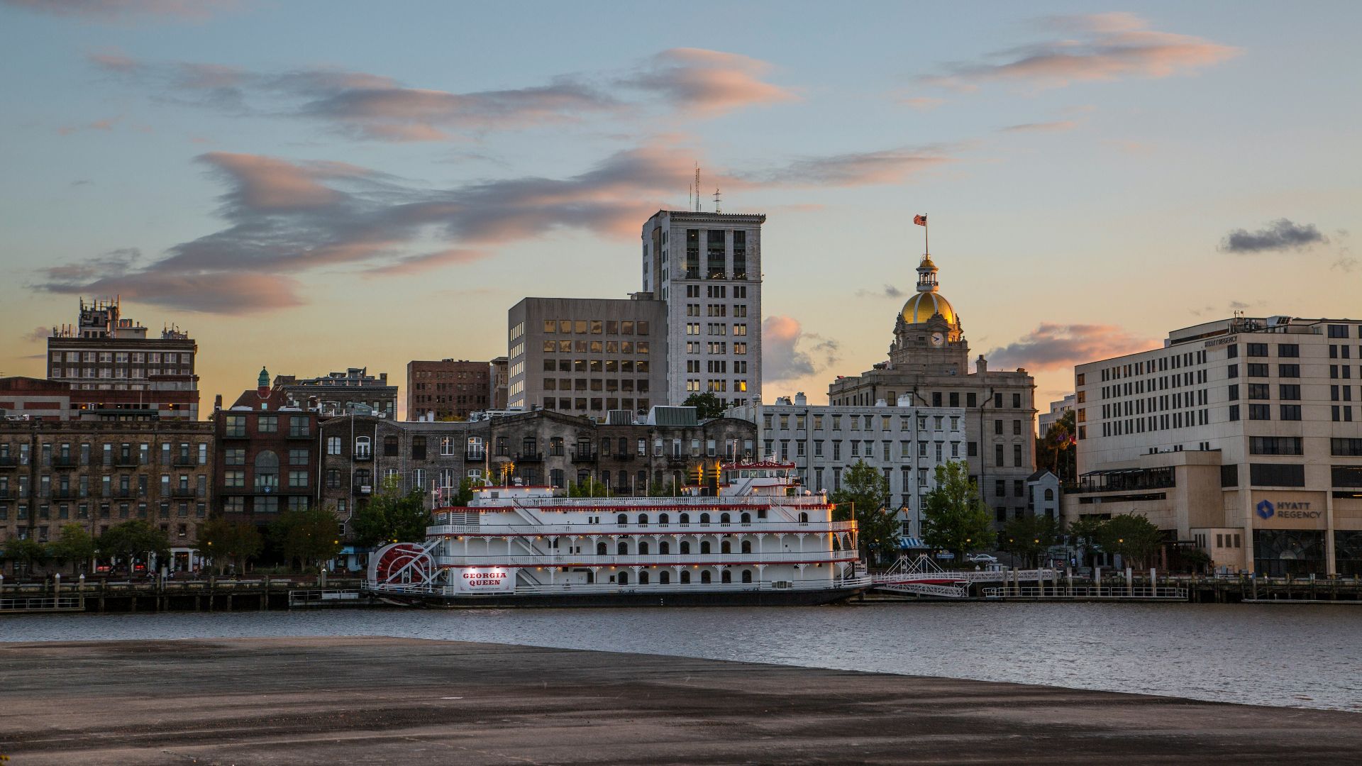white and brown boat on sea near city buildings during sunset