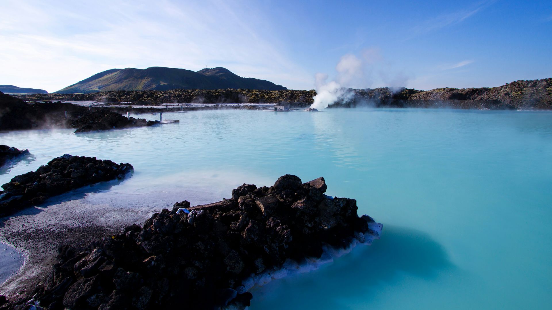 calm water beside mountain under white clouds and blue sky
