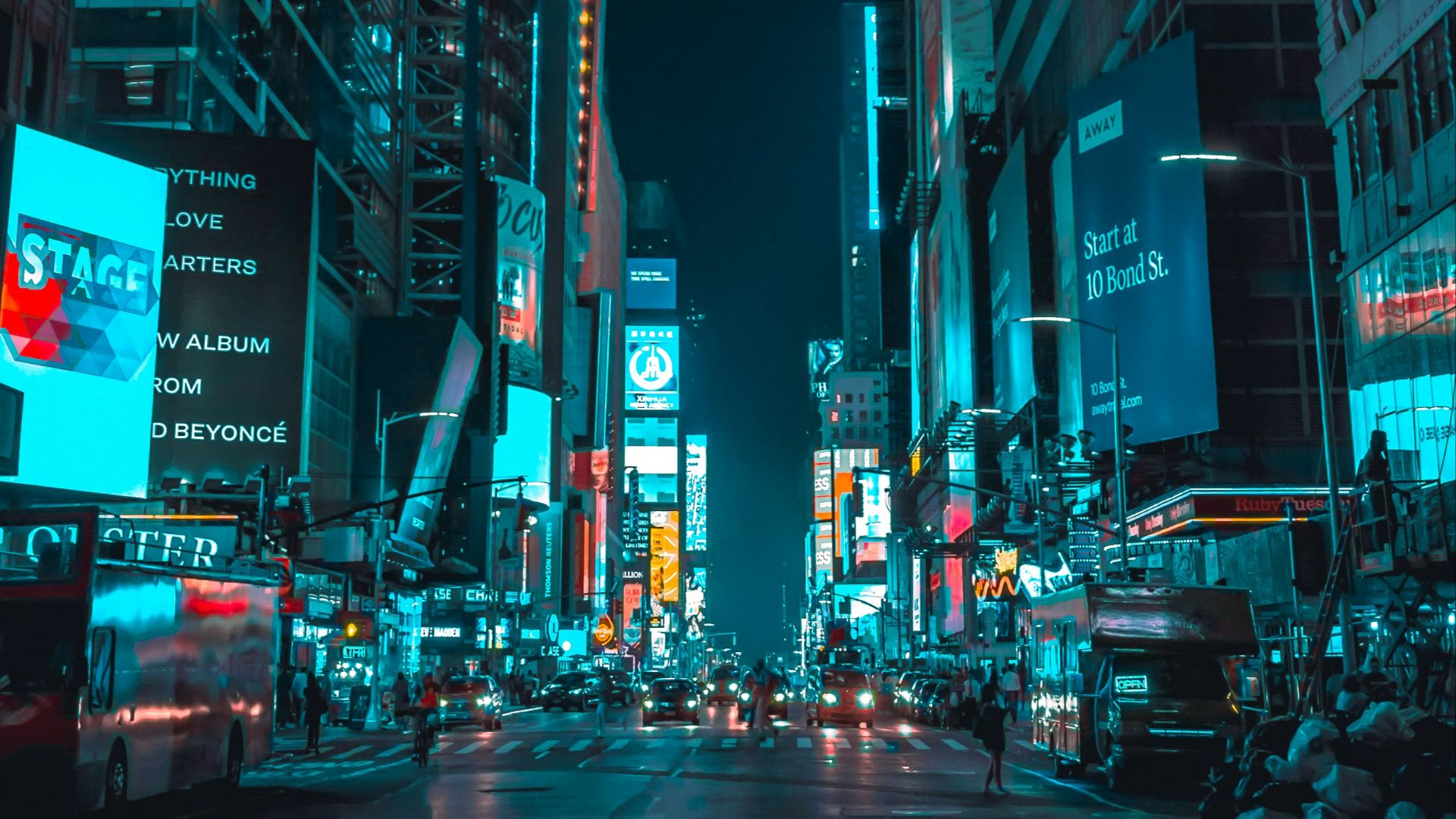 street photography of vehicles traveling on road between large buildings during nighttime
