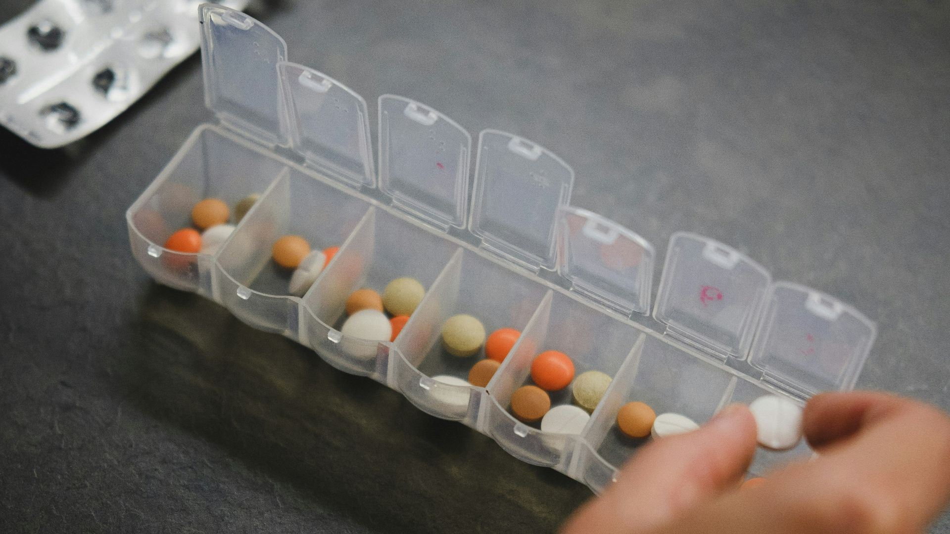 person about to pick medicine from medicine organizer