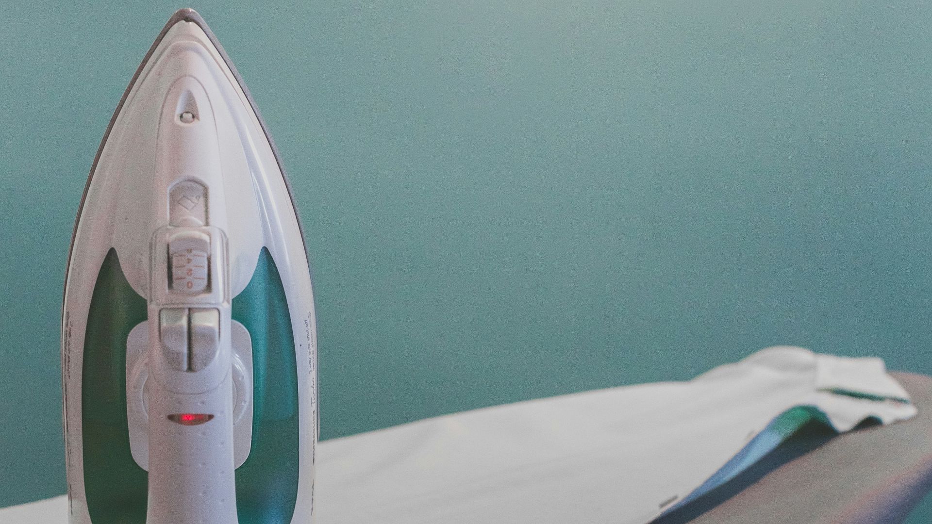 white and teal steam clothes iron plugged on ironing board