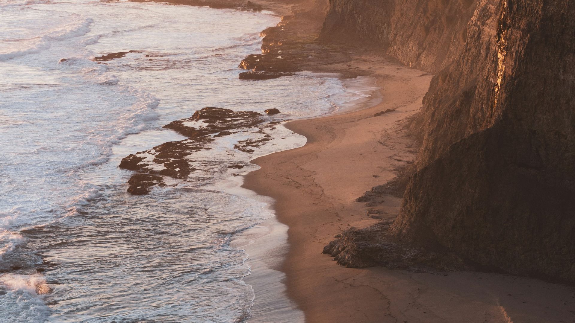 brown rocky mountain beside sea during daytime