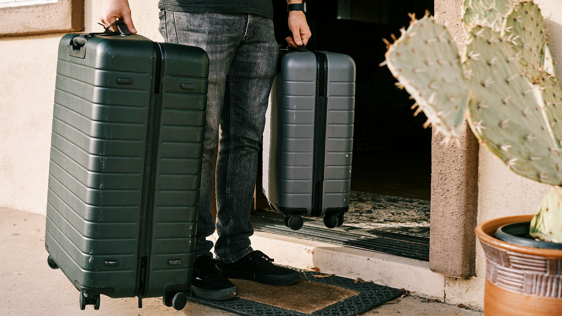 man in black denim jeans and black leather shoes standing beside black luggage bag