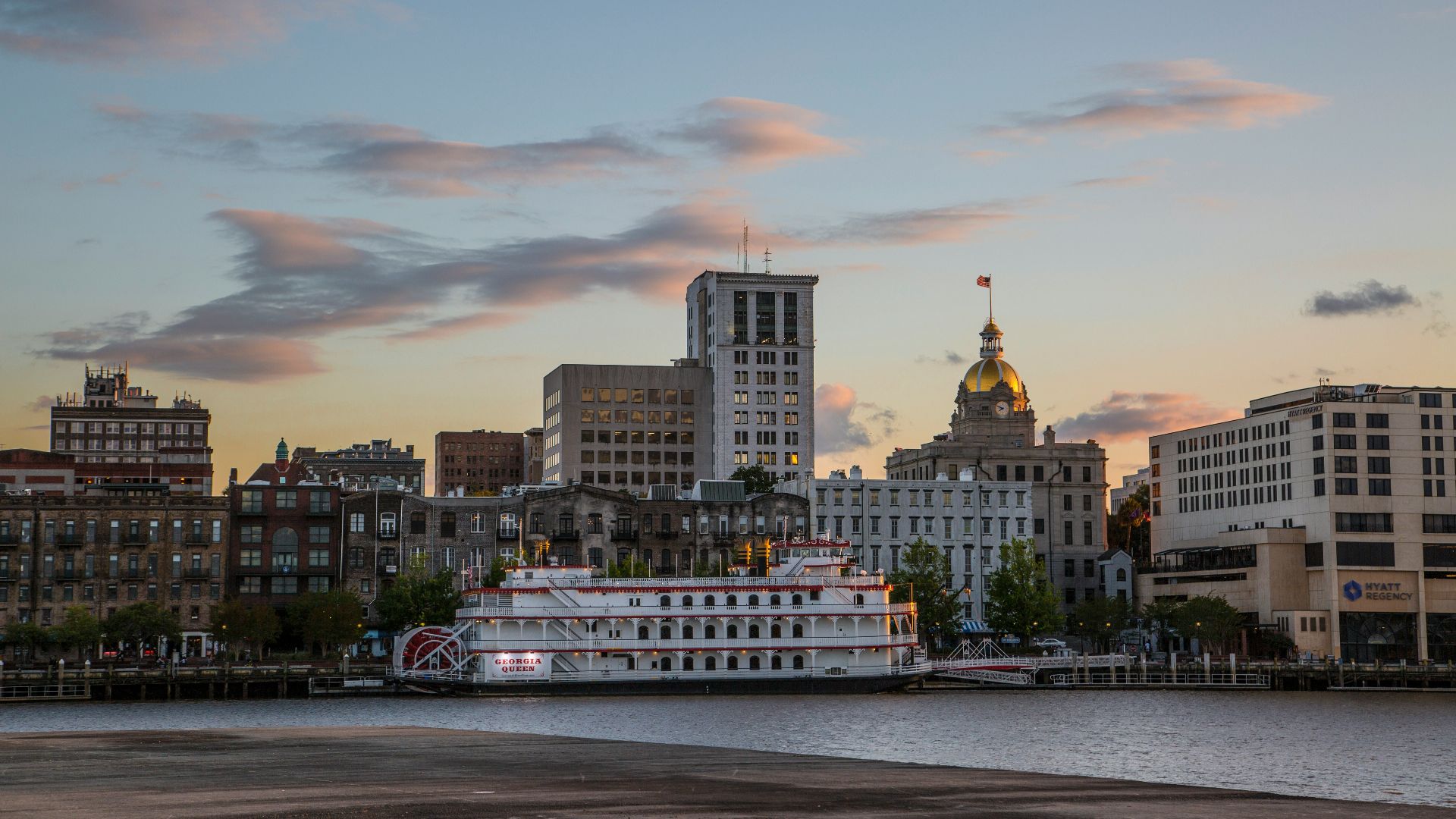 white and brown boat on sea near city buildings during sunset