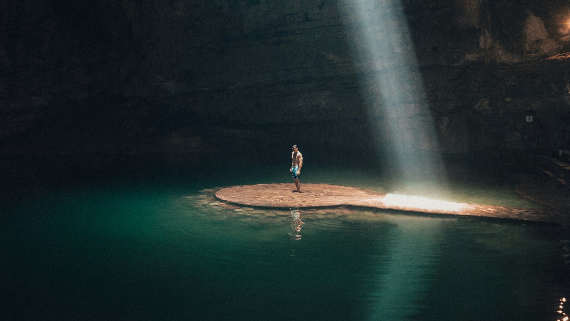 photo of man standing in cave surrounded by water