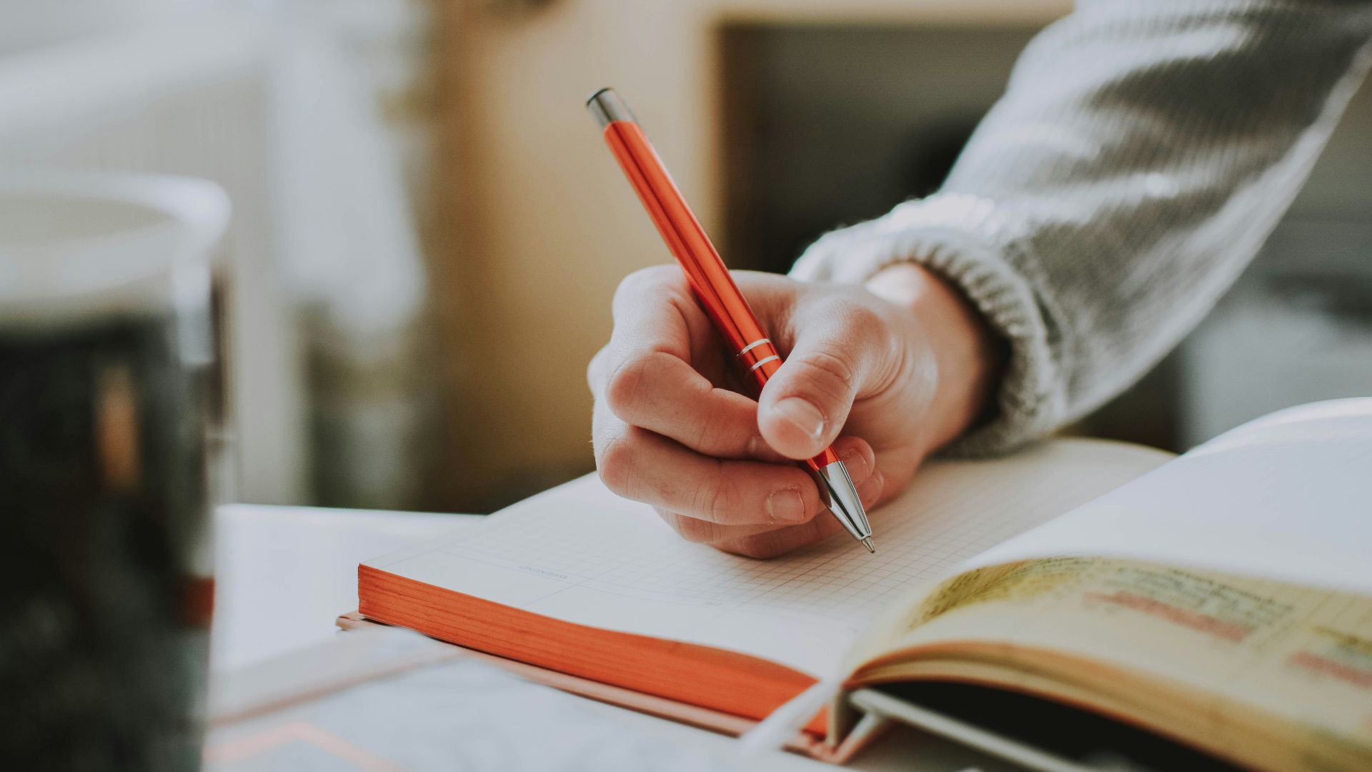 person holding on red pen while writing on book