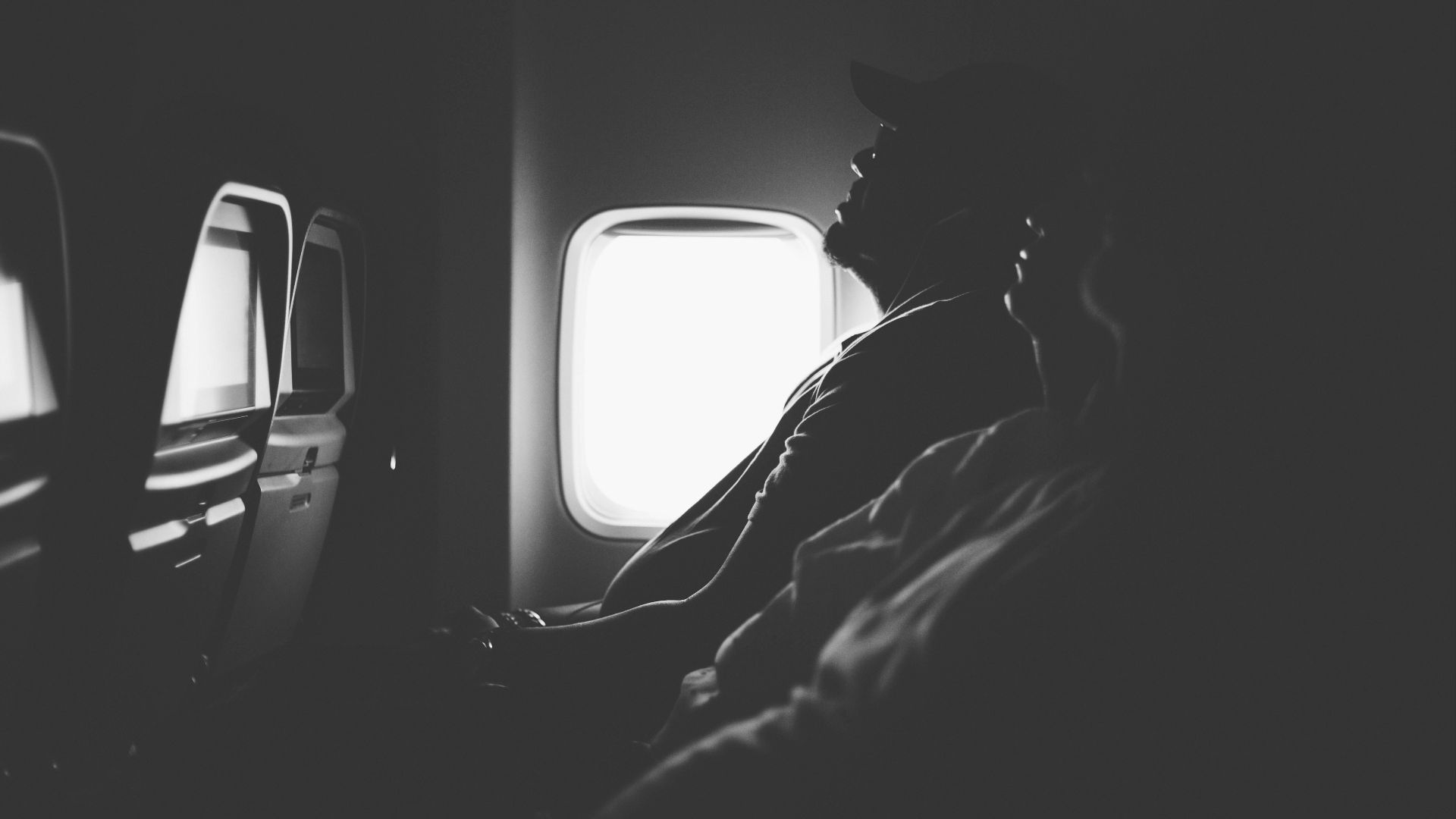 grayscale photo of three person sitting inside airplane