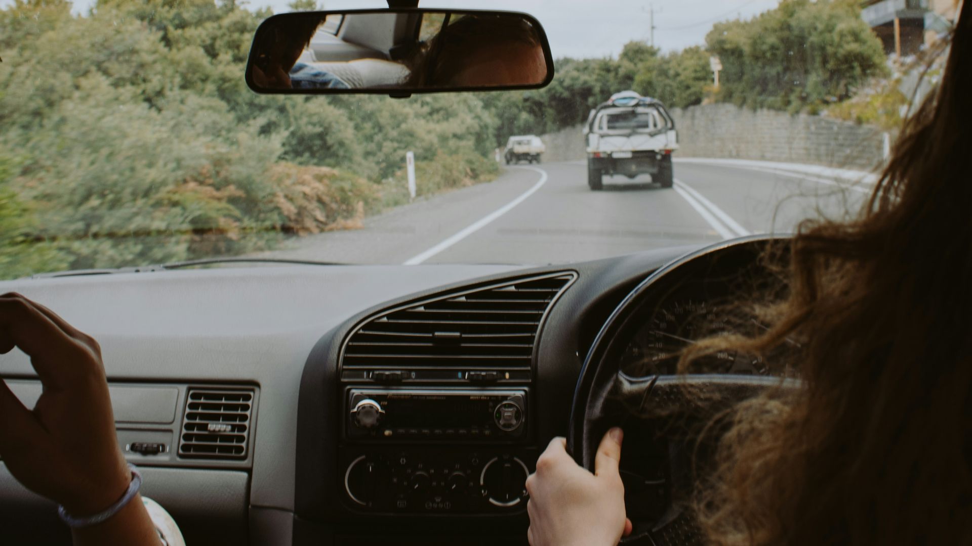 woman driving car on tree lined road during daytime