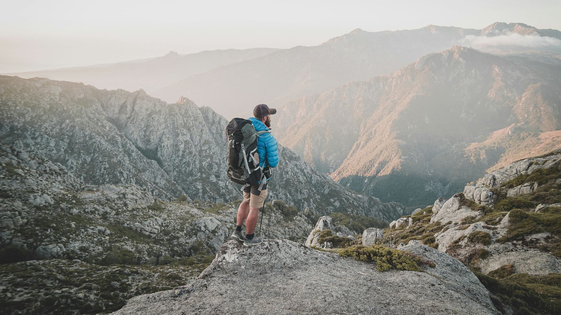 man in blue t-shirt and black shorts with hiking backpack walking on rocky mountain during