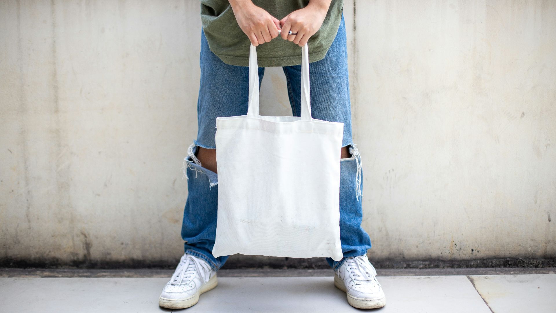 person in blue denim jeans holding white tote bag