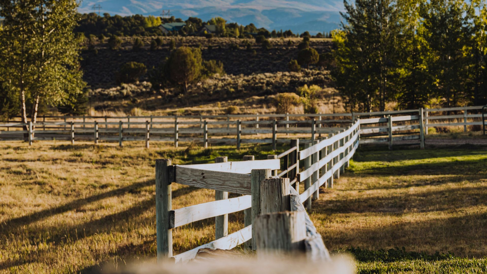 a wooden fence in a field with mountains in the background