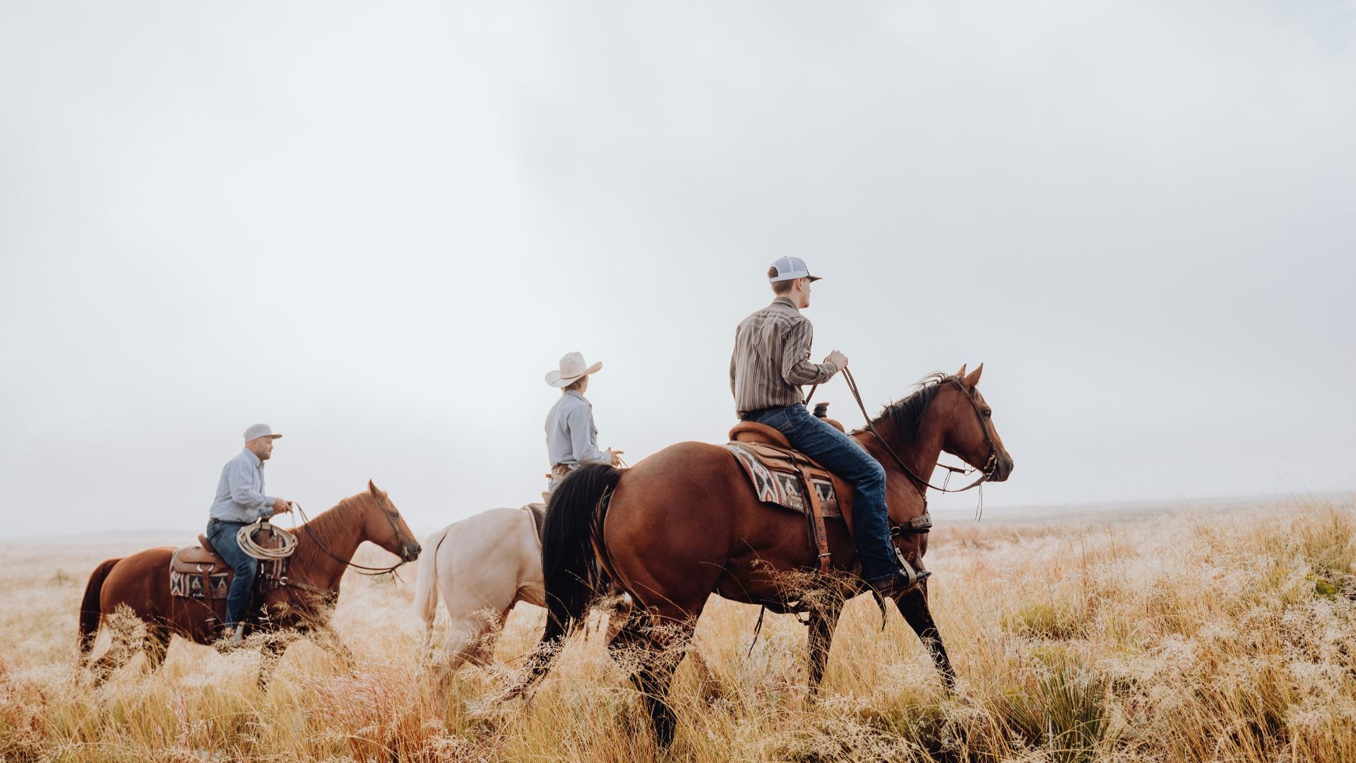 three people riding horses through a dry grass field