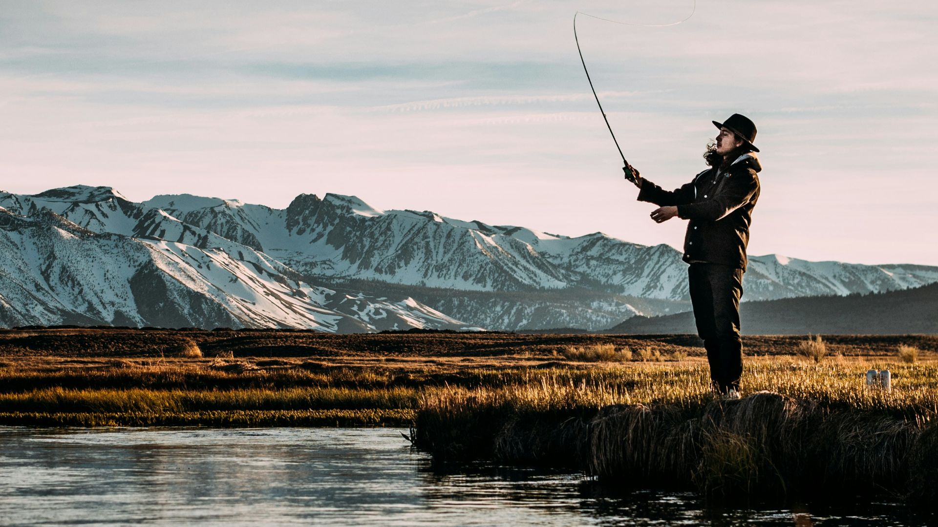 landscape photo of man fishing on river near mountain alps