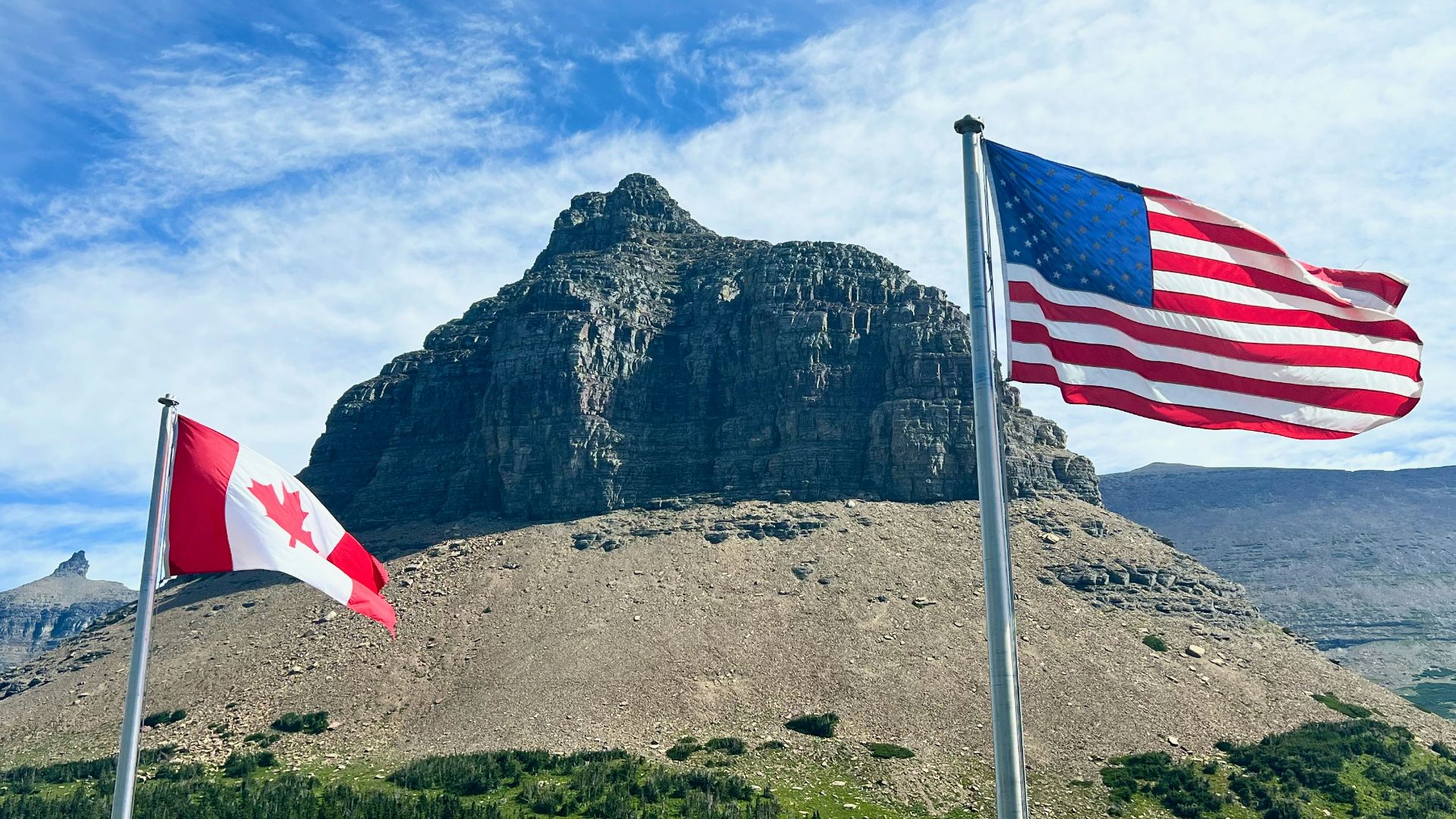 two american and canadian flags flying in front of a mountain