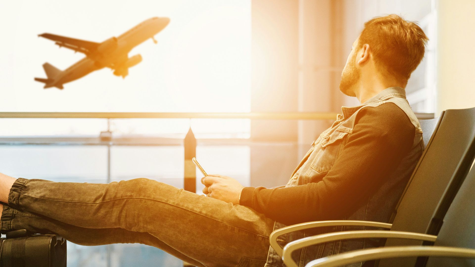 man sitting on gang chair with feet on luggage looking at airplane