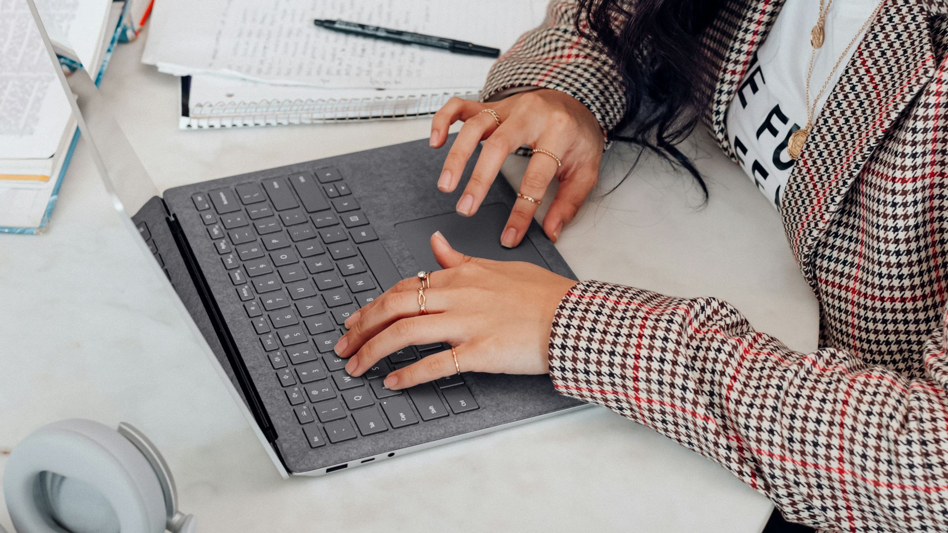 woman in red and white plaid long sleeve shirt using platinum coloured microsoft surface laptop computer