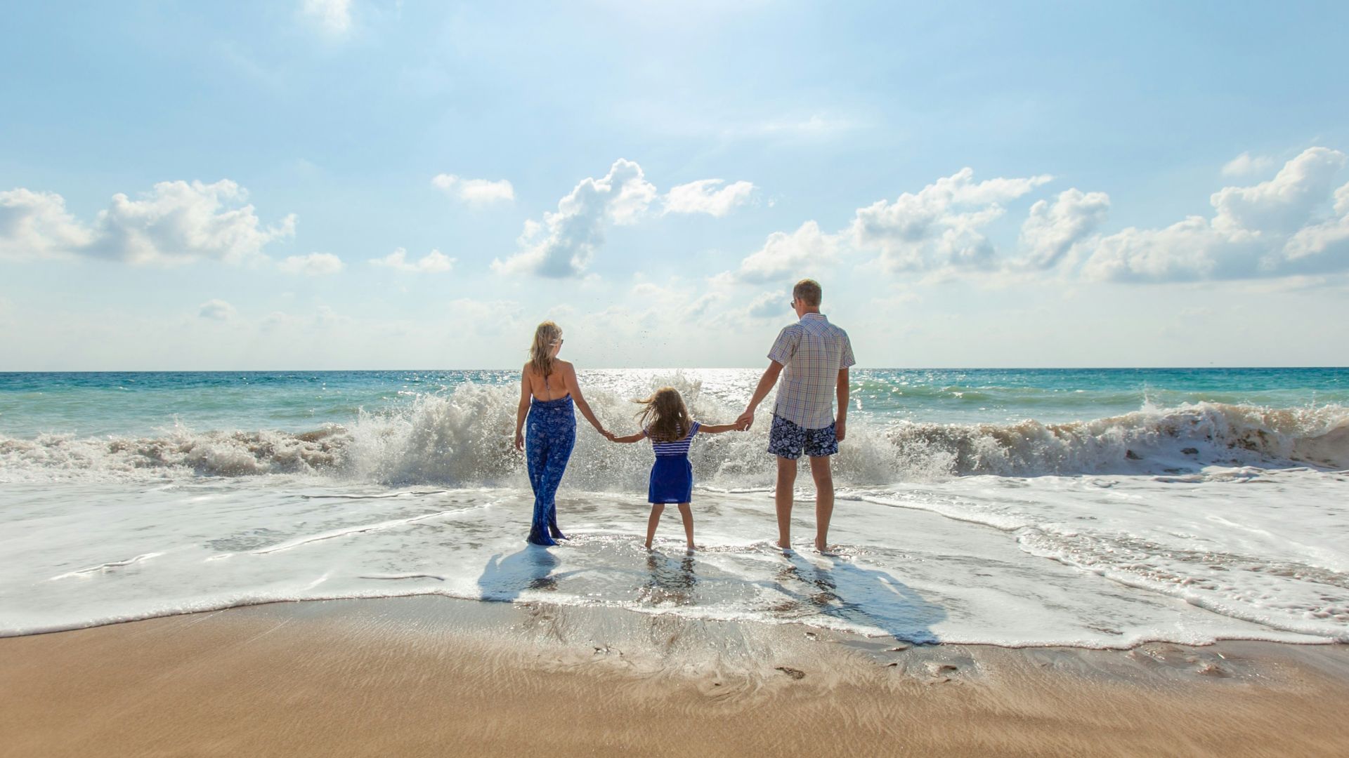 man, woman and child holding hands on seashore