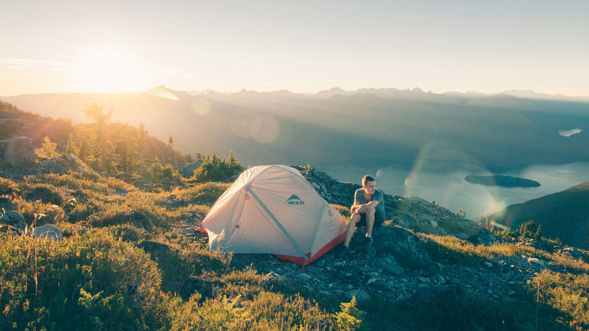 man sitting on stone beside white camping tent